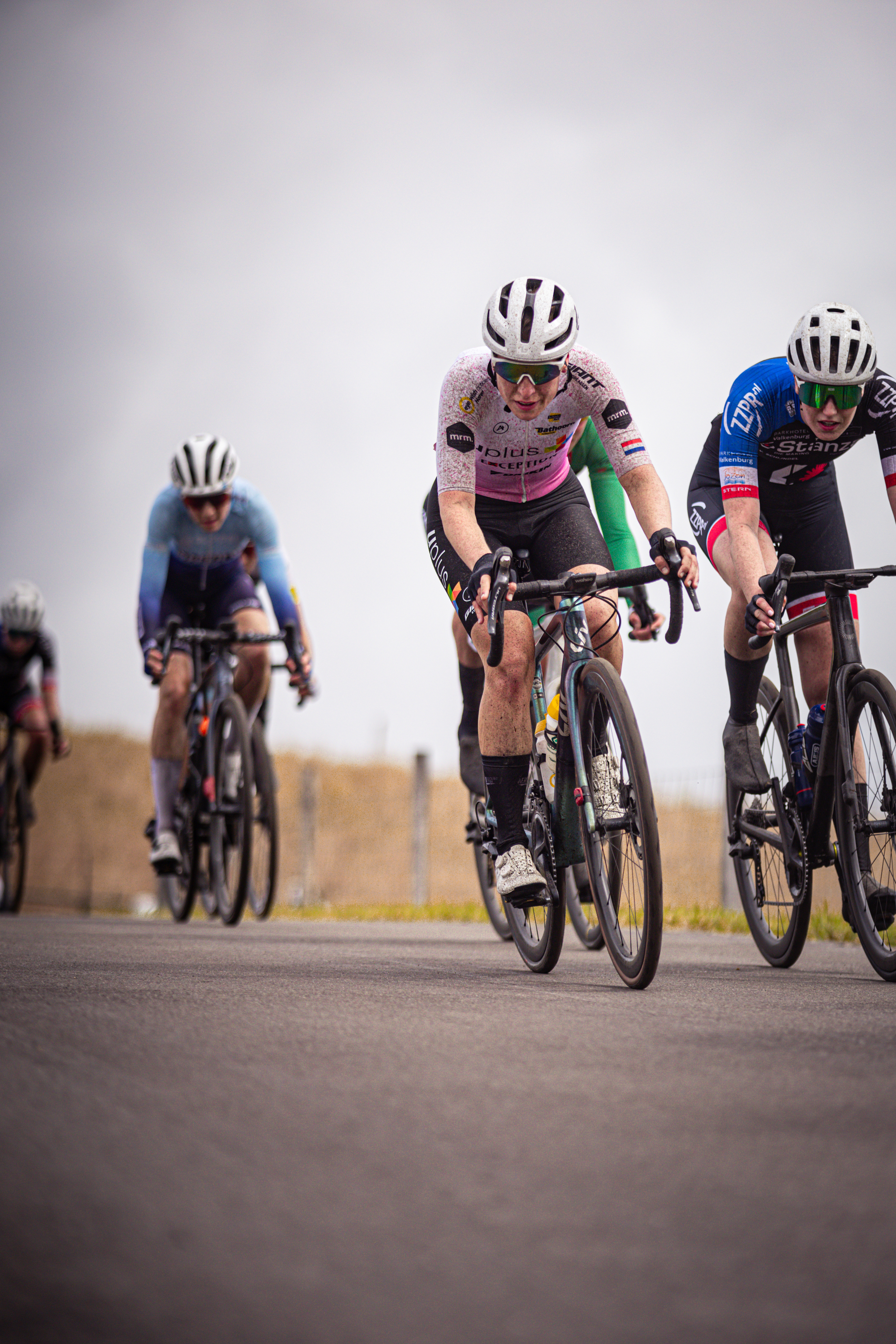 Three cyclists are wearing helmets and racing on a road.