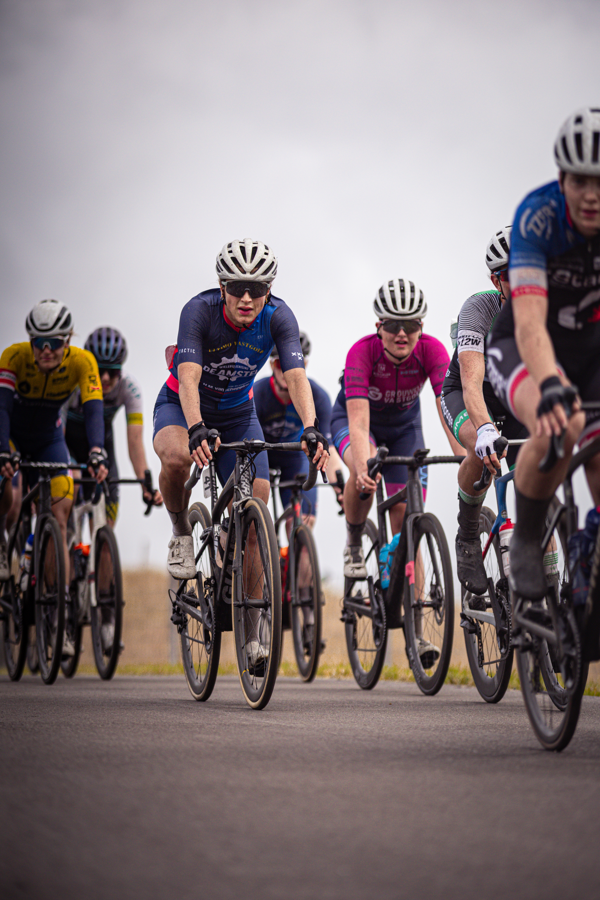 Several bicyclists are riding through a field of grass with the leader wearing pink.