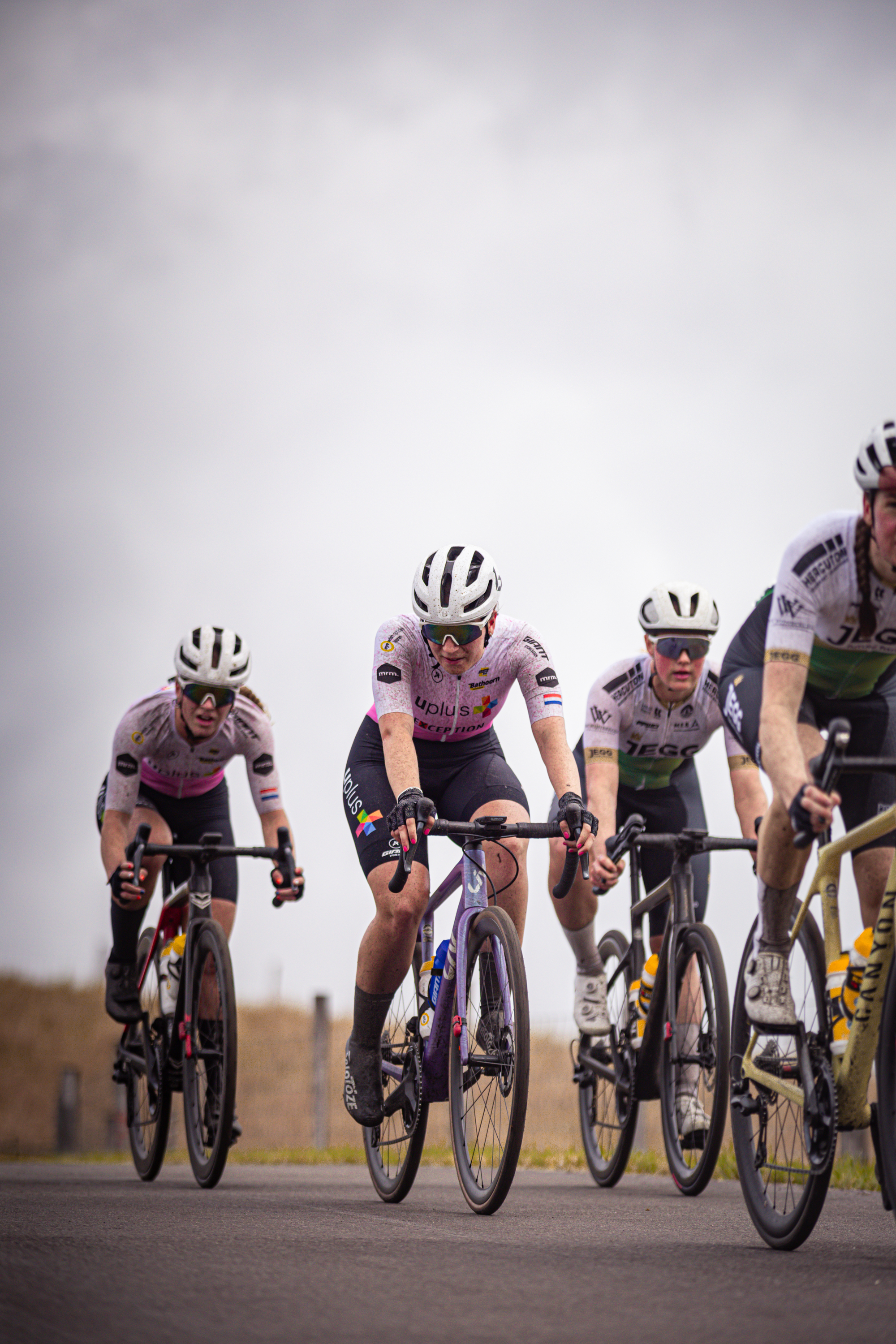 Four cyclists riding on a road in black, white and pink uniforms.