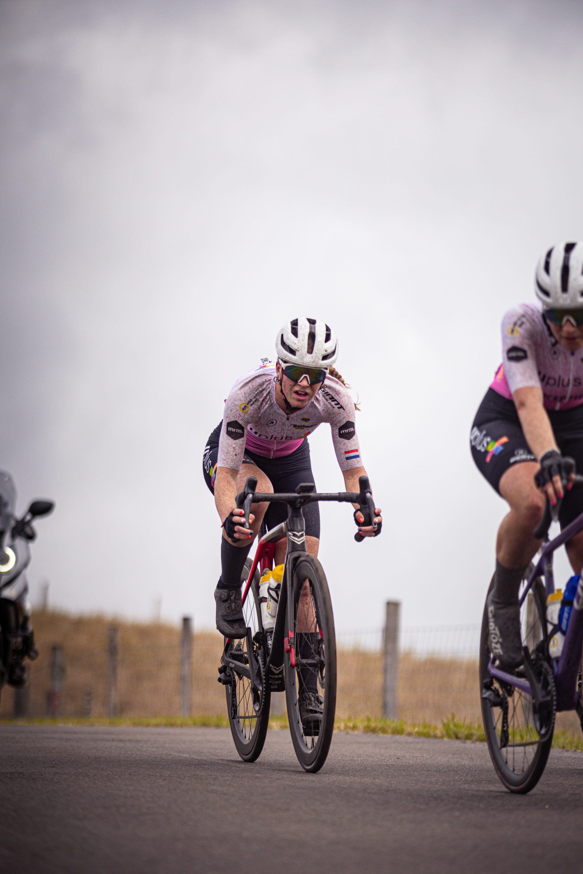 Two professional cyclists on a race track. The cyclist in the lead is wearing black shorts and has the number 4 on her back.