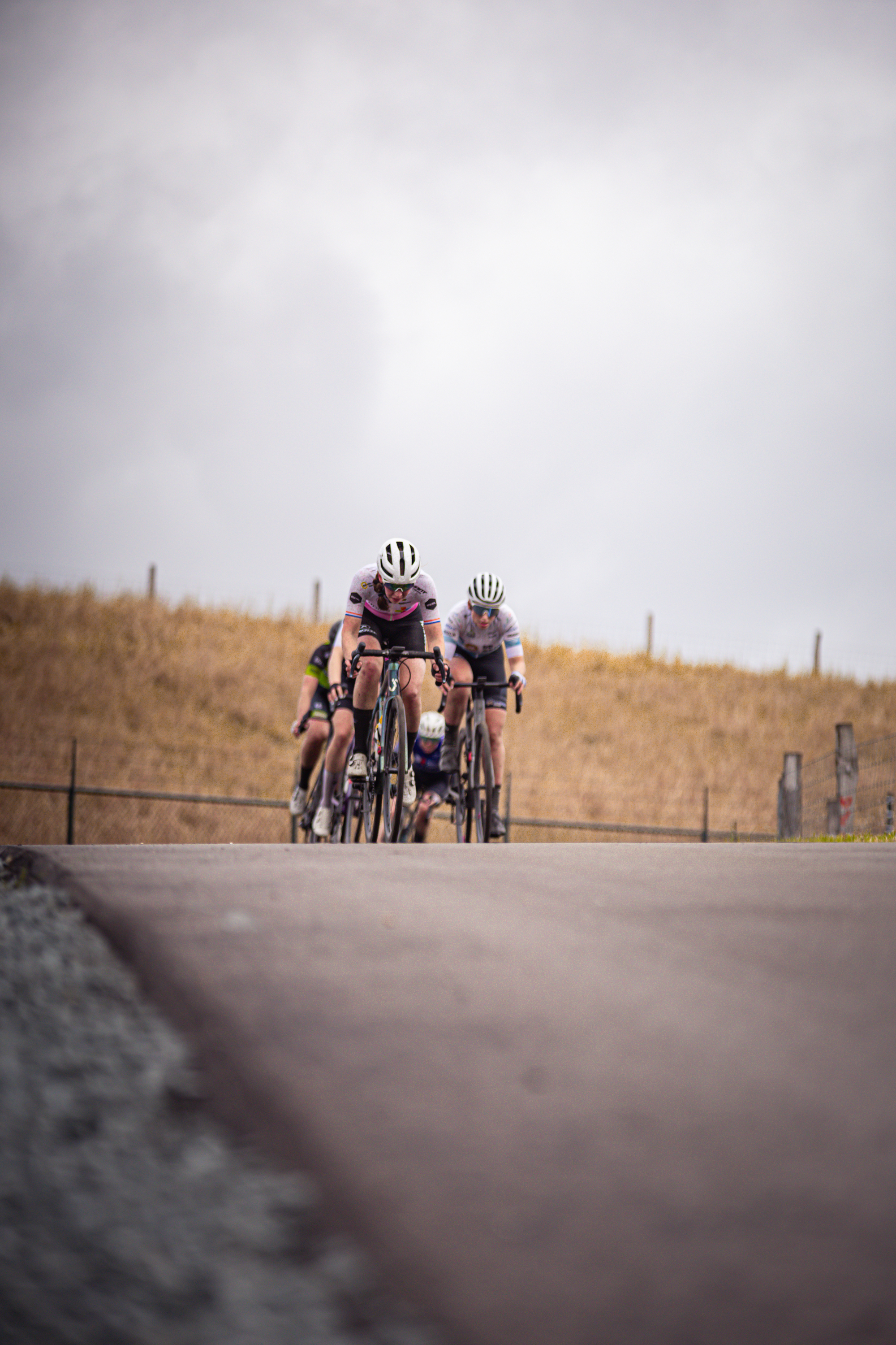 Two cyclists race on a road, with a pink cyclist leading the way.