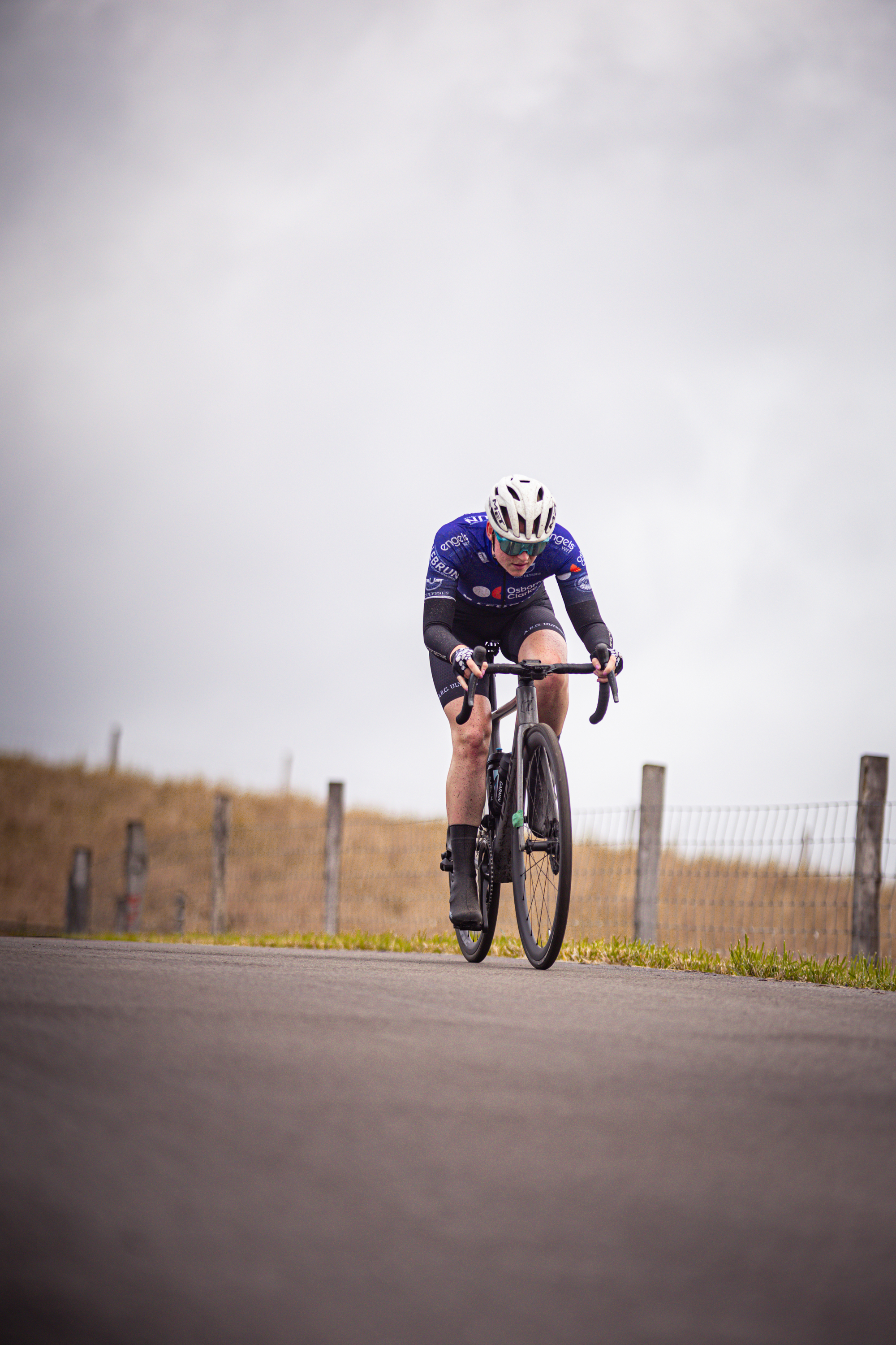 A woman wearing a black, blue and white jersey is riding a bicycle.