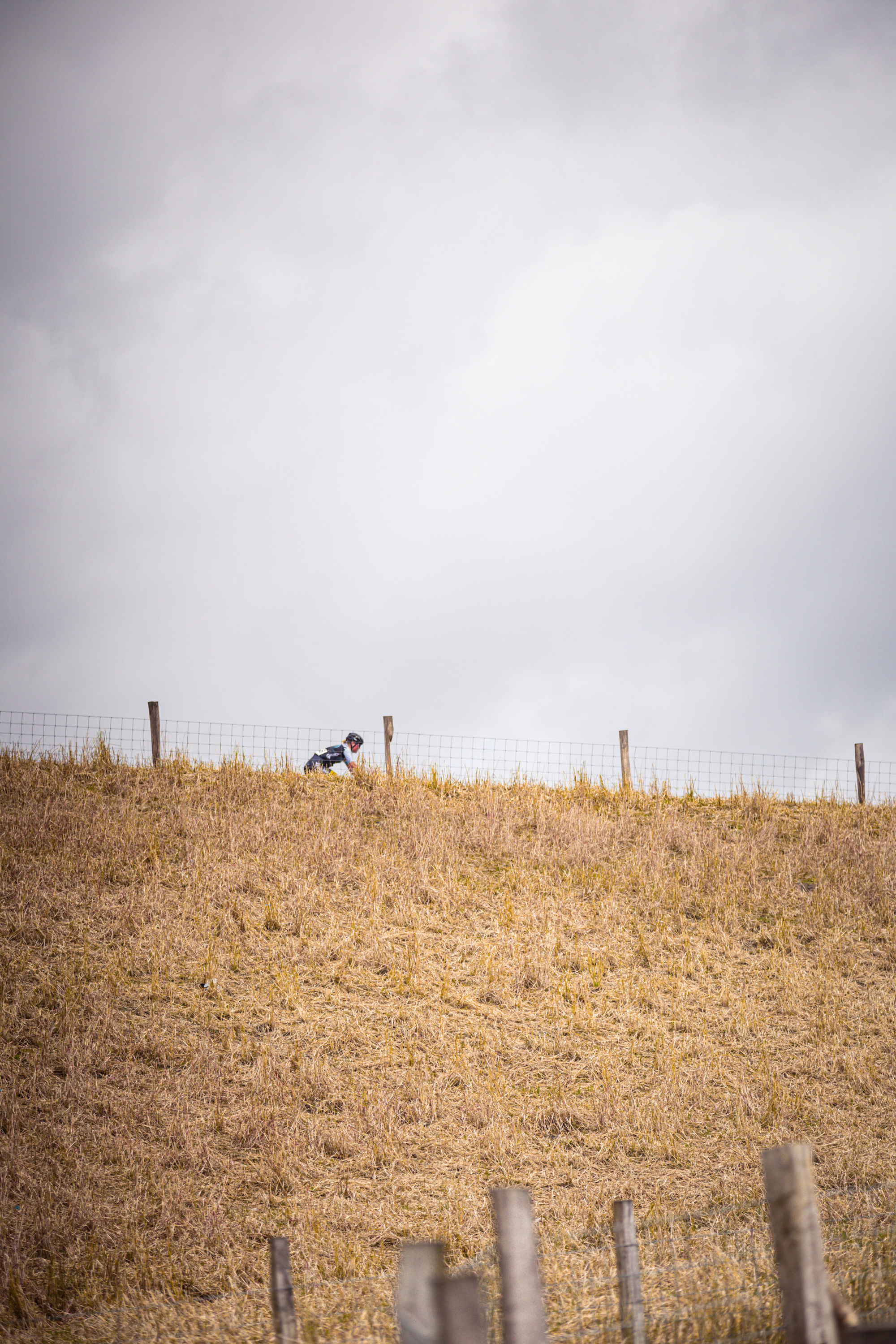 A man is riding his bicycle on a grassy hill that has a barbed wire fence at the top.