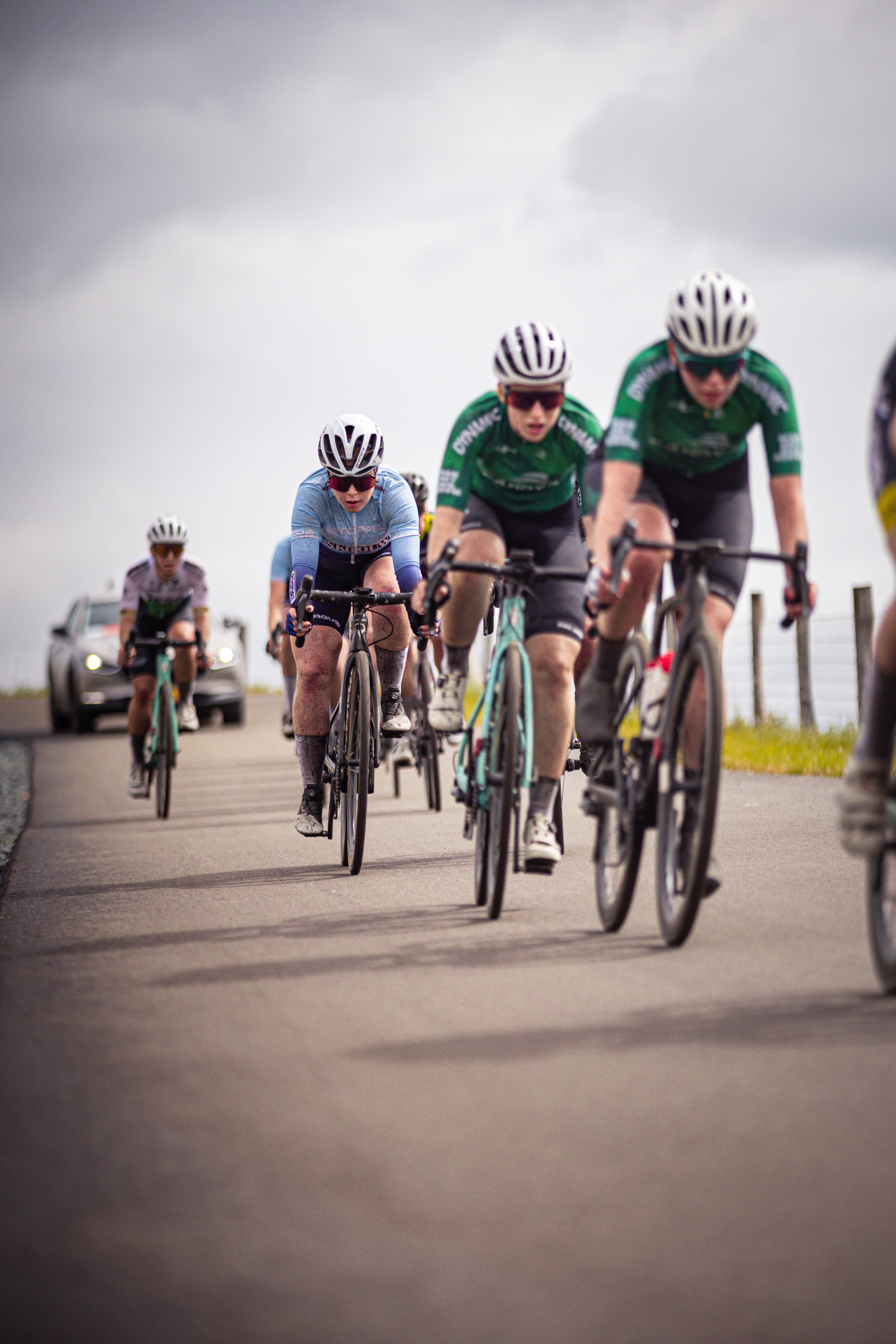 A group of cyclists racing through a road. The lead cyclist is wearing a green jersey with the number 5 on it.