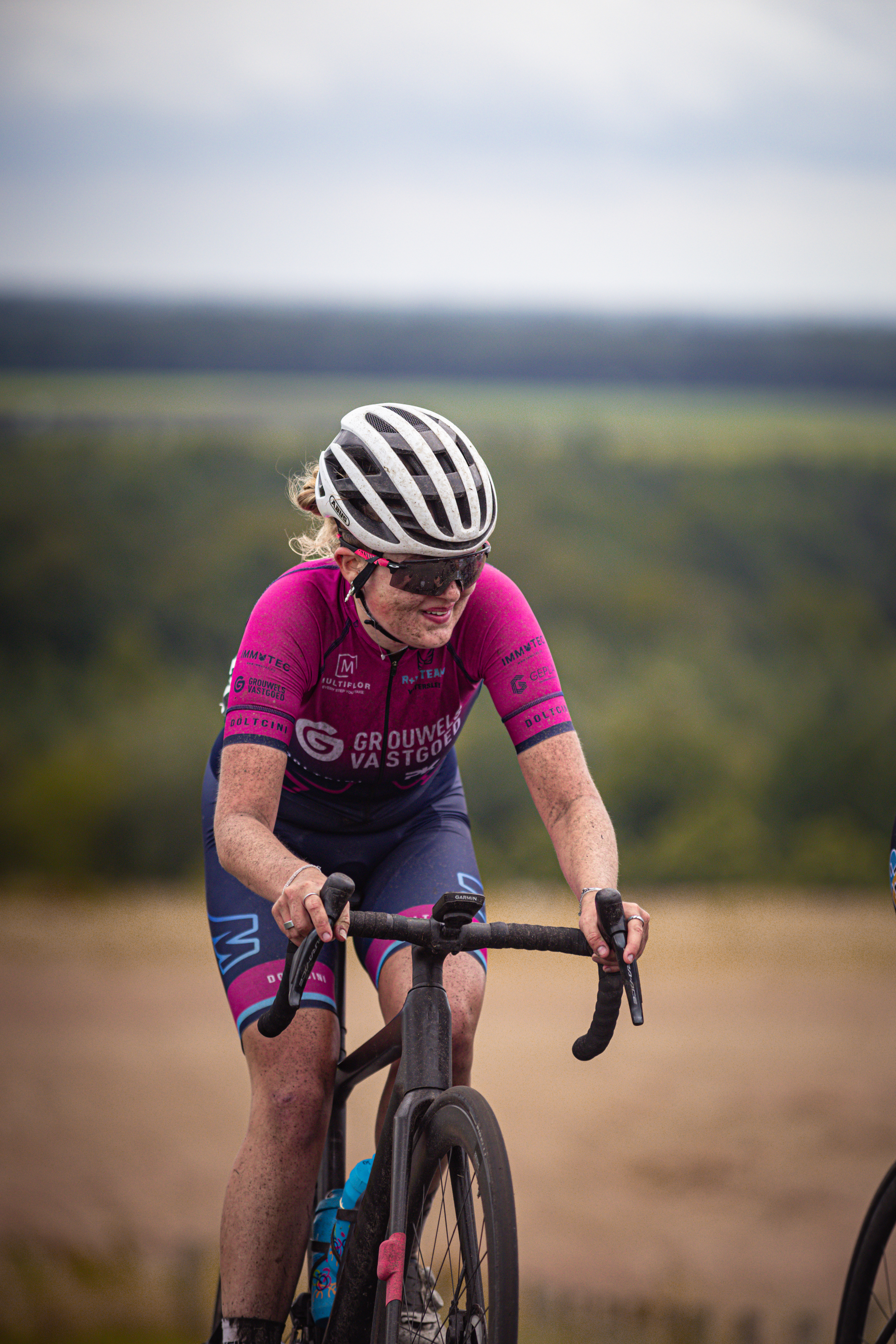 A woman wearing a pink and purple cycling outfit riding on a bicycle.