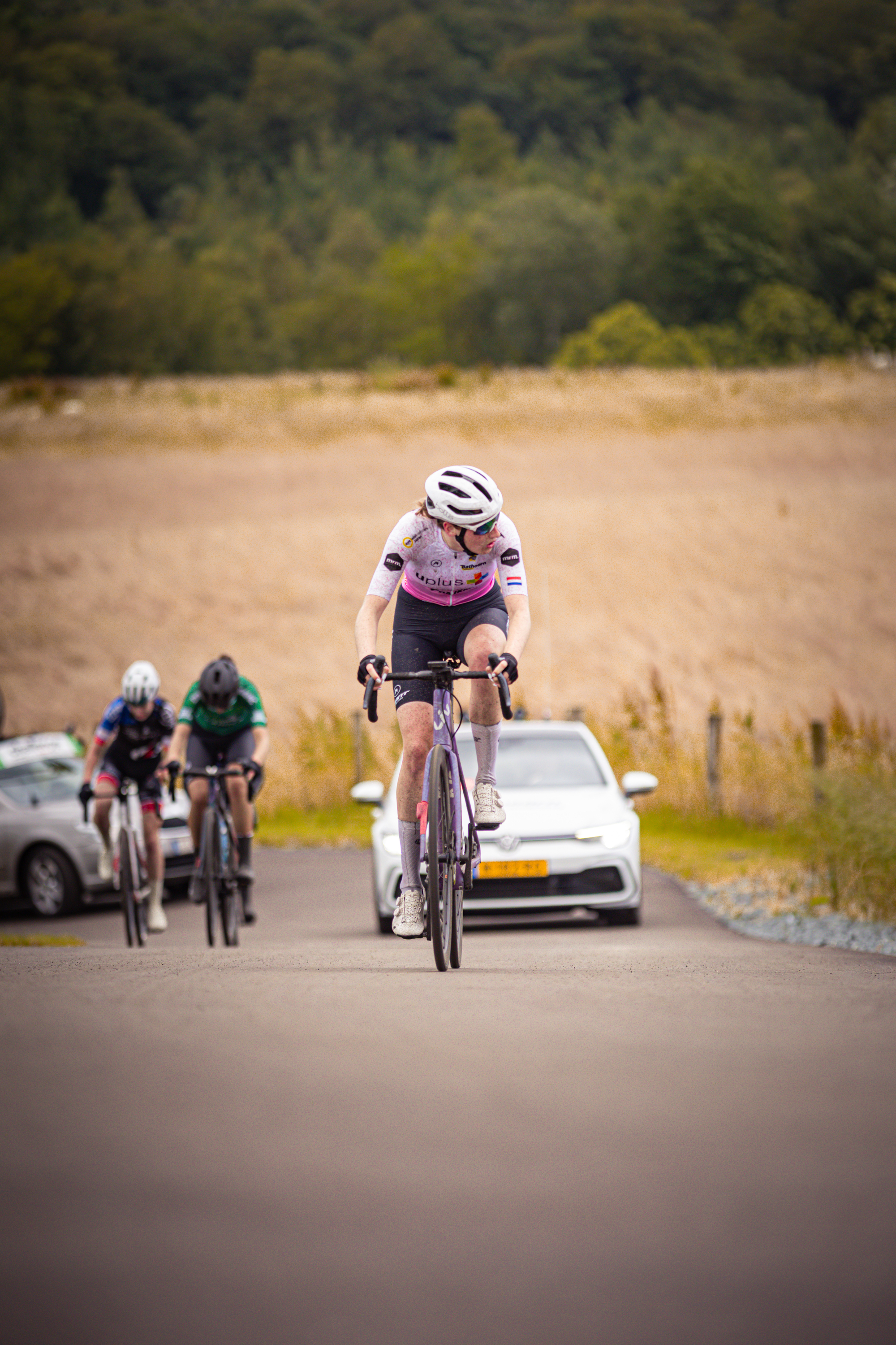 Three cyclists riding down the road, one with 2024 on her helmet.