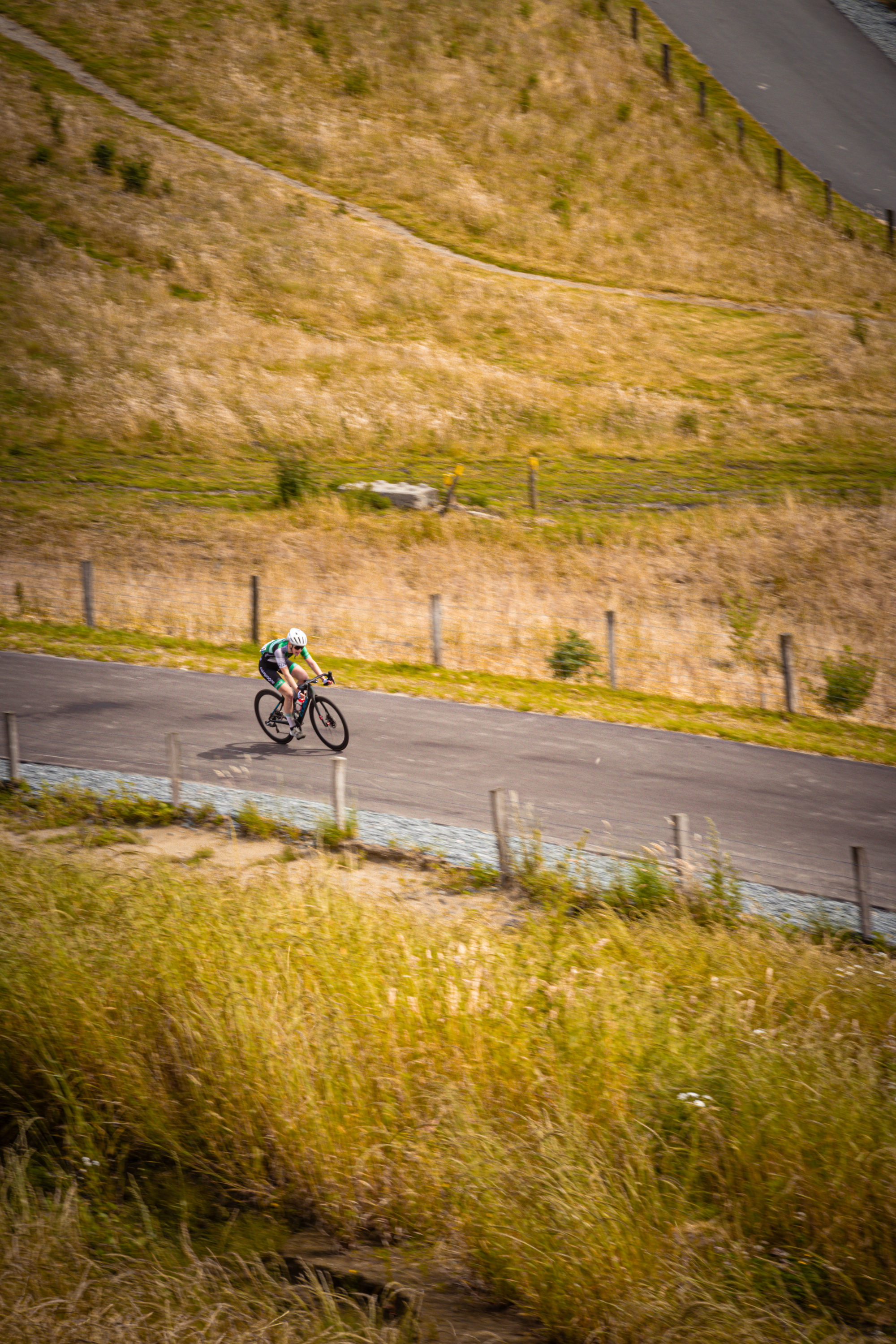 "Female cyclist wearing a white jersey and riding a black bike on the side of the road."