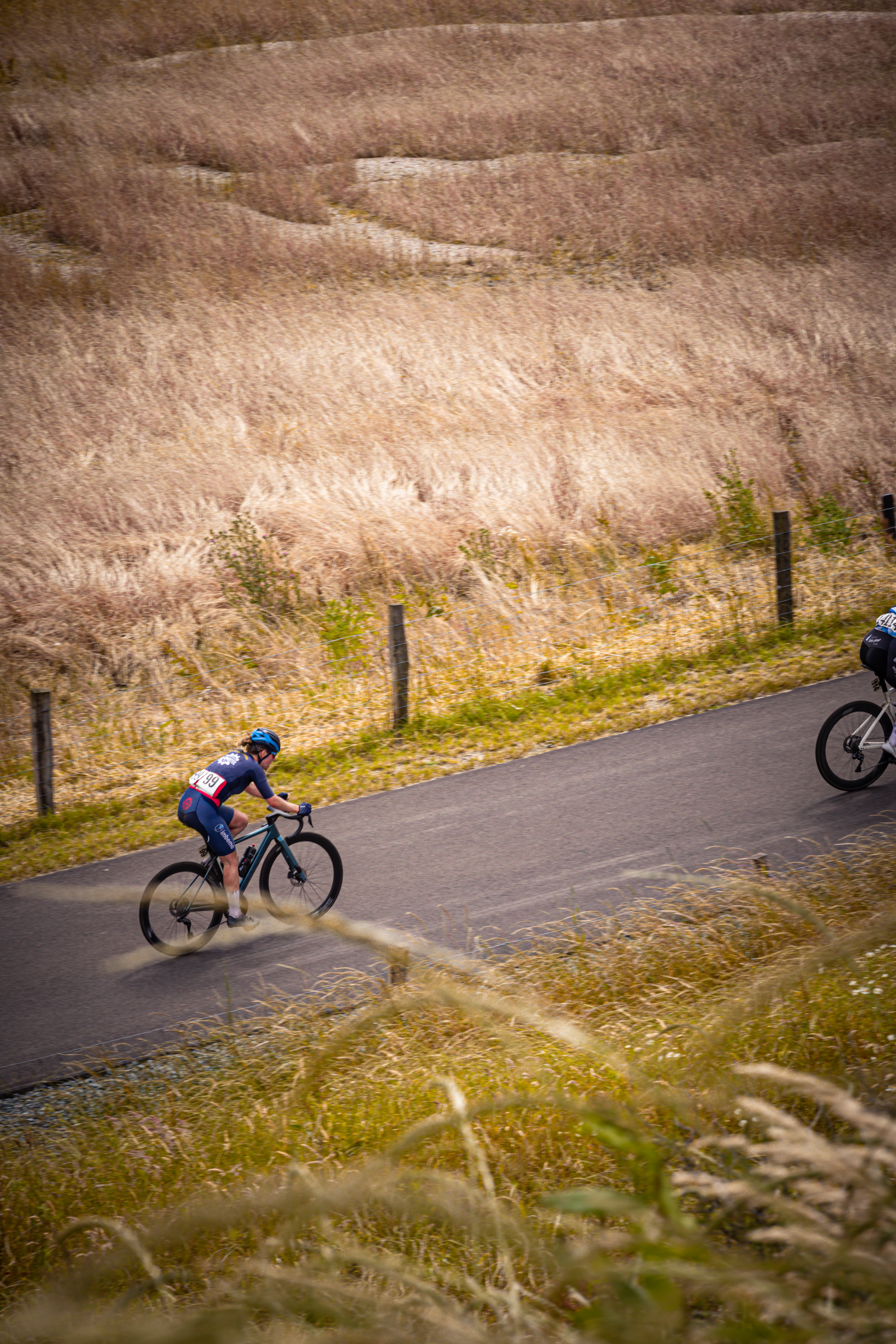 A cyclist racing on a road with another cyclist in the background.