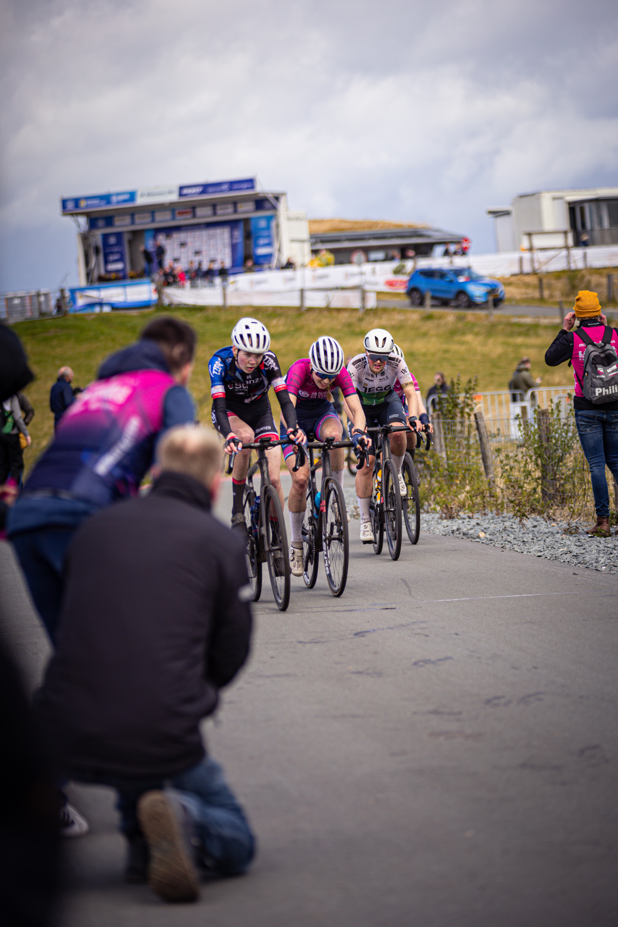 A group of cyclists race down a street in front of a crowd.