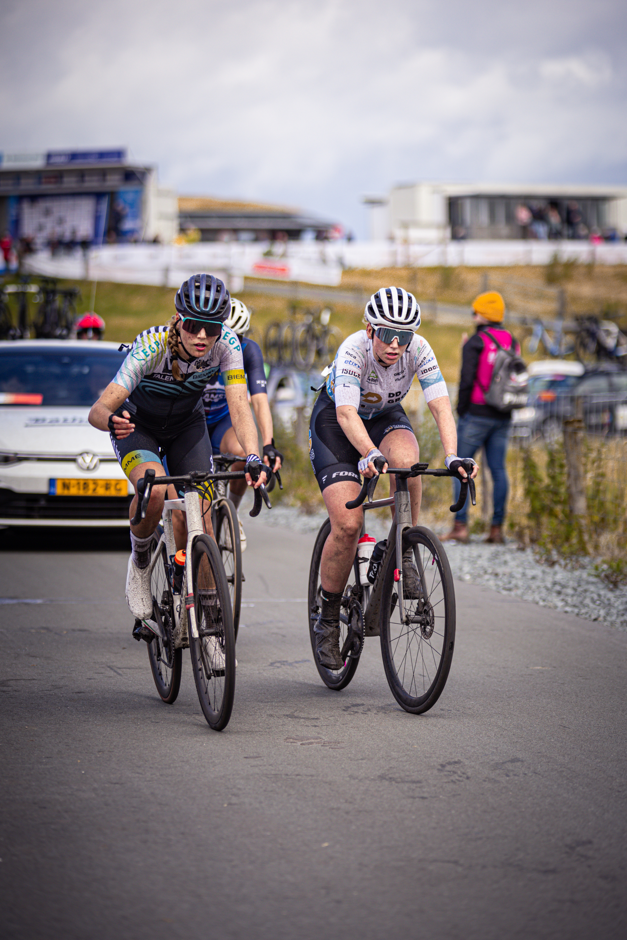 Two cyclists wearing matching uniforms race down a street.