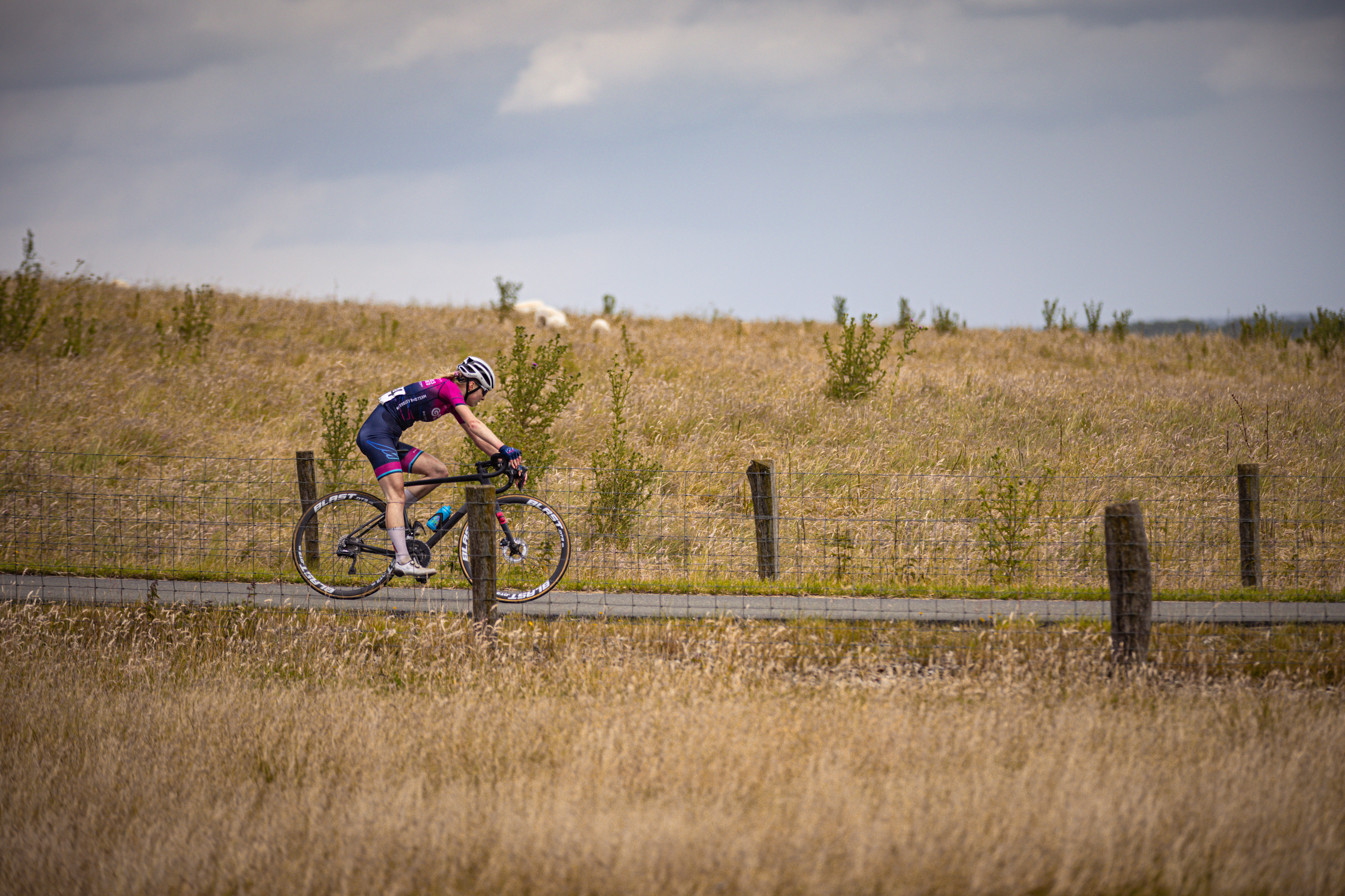 A woman on a bike in the middle of the desert, riding through tall grass.