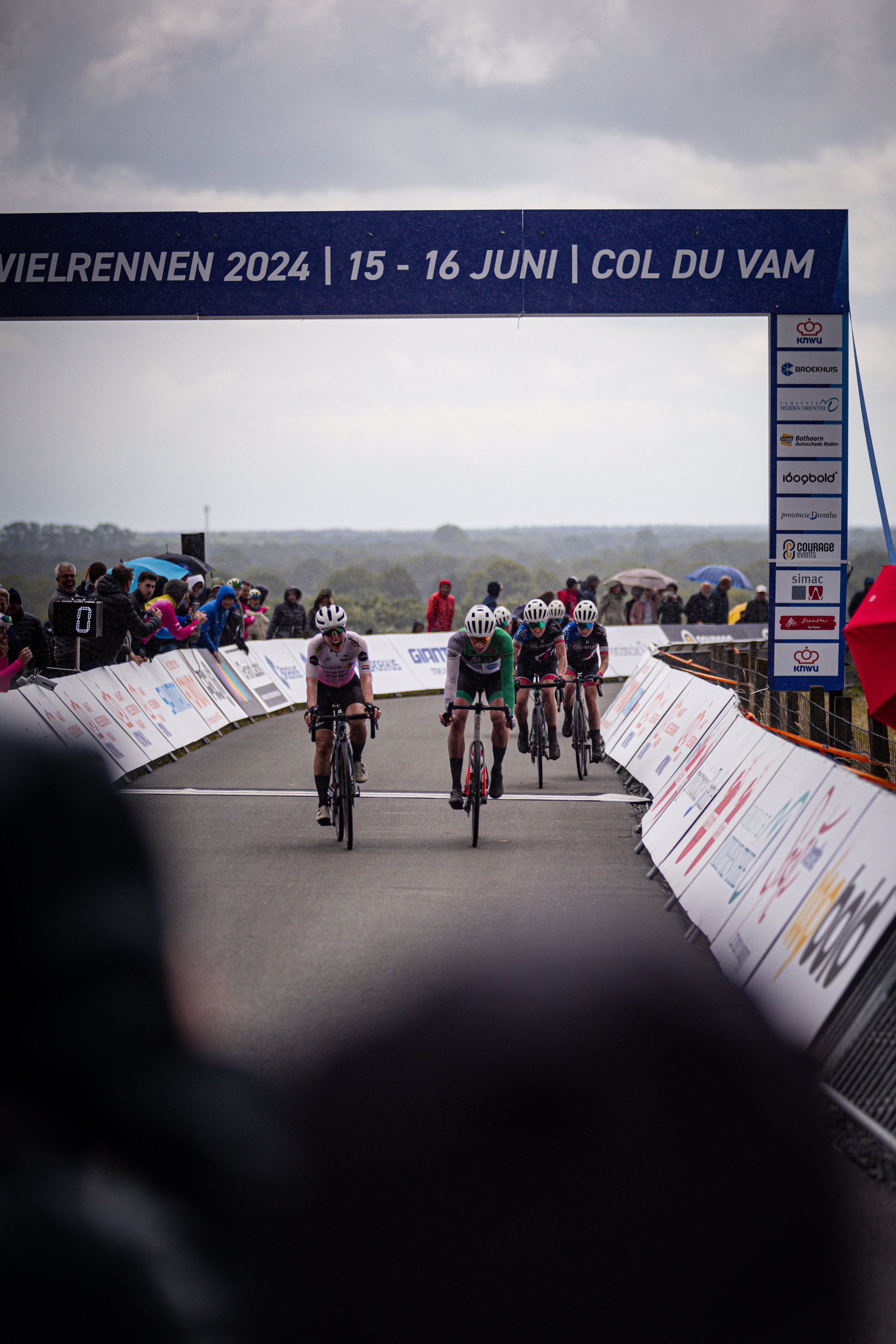 A bicycle race is taking place on a course named "Wielrennen". The word "Col du Vam" is also visible at the top of the image.