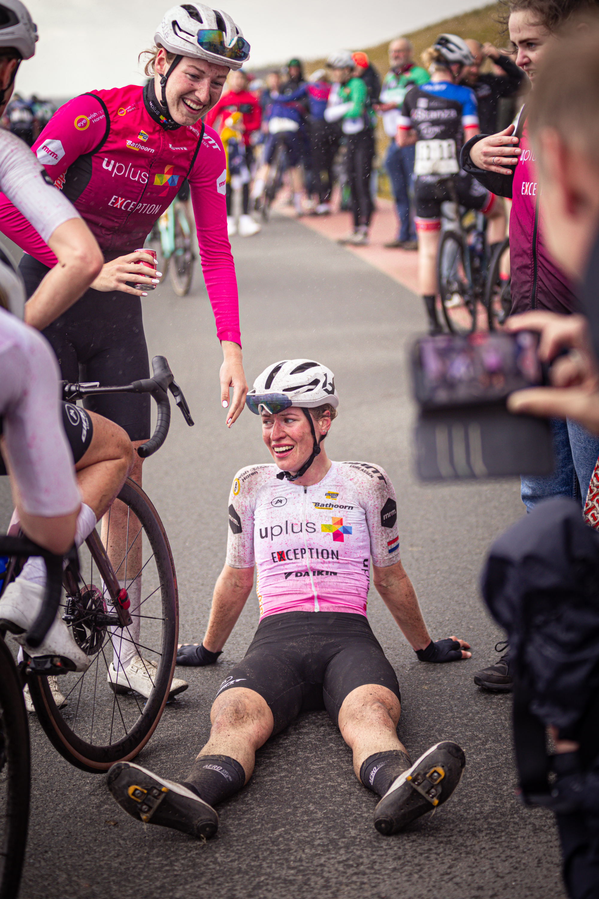 Two women on a bicycle, one is wearing a pink jersey with the number 1 on it and smiling at someone.