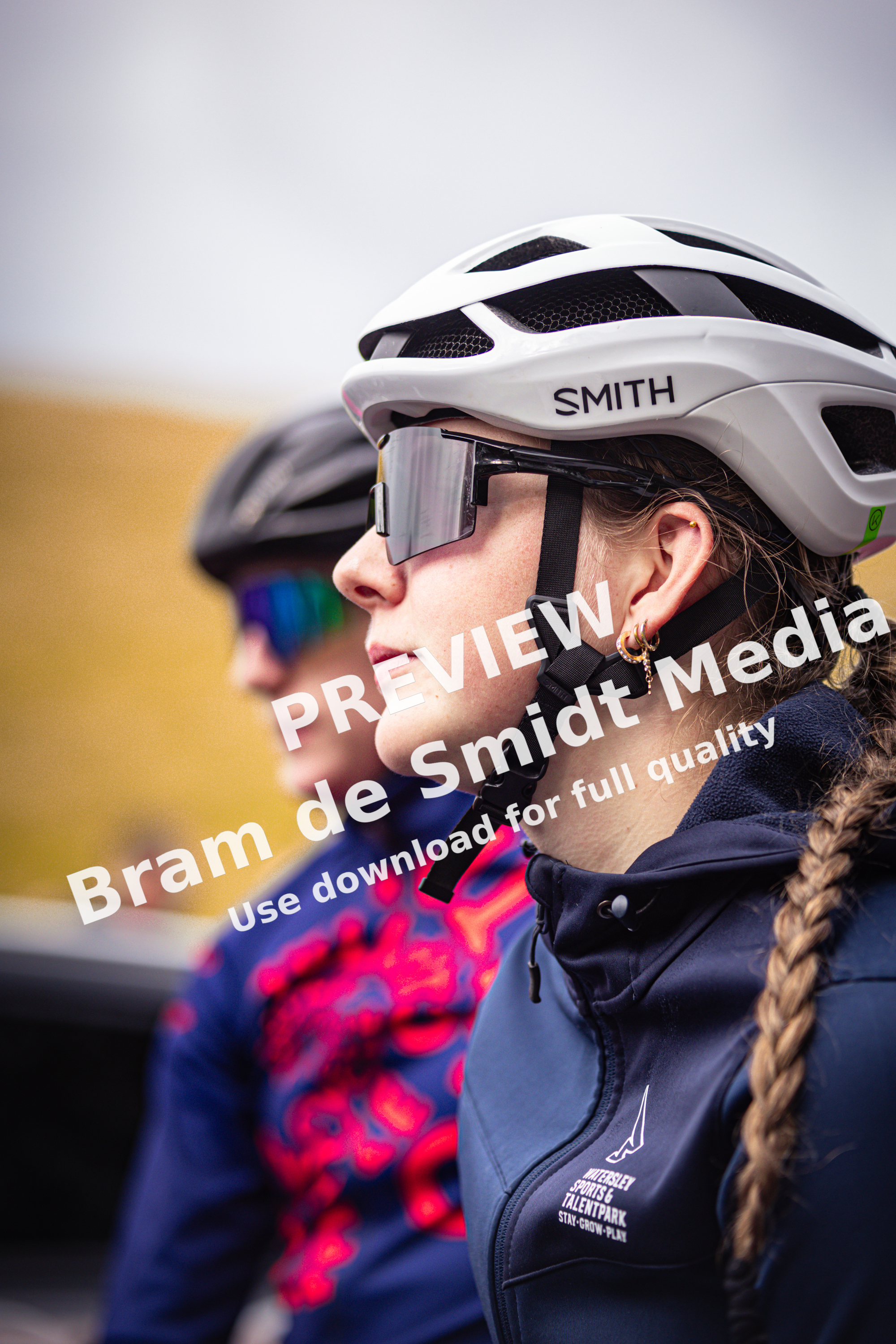 Two women wearing a helmet and goggles, with the woman in the foreground wearing sunglasses on top of her helmet.