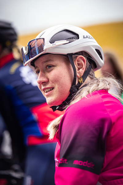 A woman wearing a helmet with the word "Luge" on it. She is also wearing a pink jacket, and she has blonde hair.