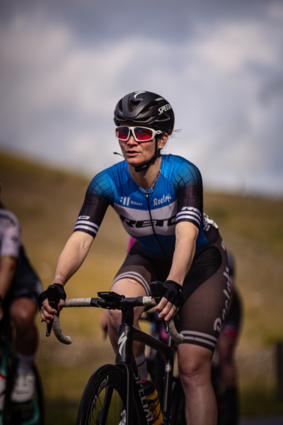 A woman is wearing a blue jersey and a black helmet as she rides her bike.