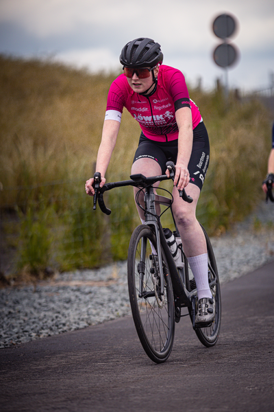 A woman wearing a red shirt and black shorts rides her bike down the road.