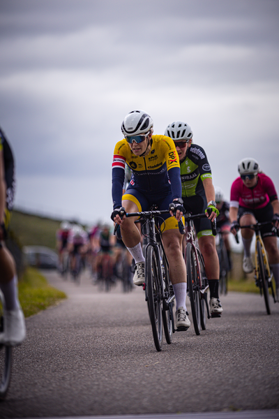 A female cyclist in a yellow jersey races alongside other cyclists on the street.