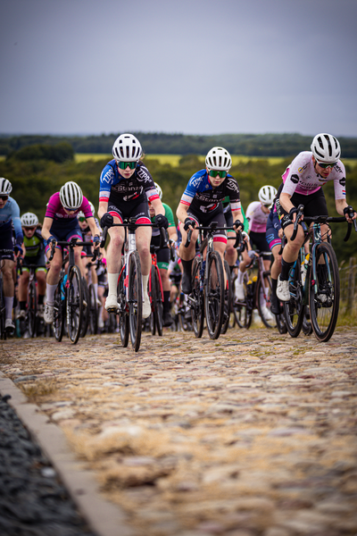 Several young women are racing on bicycles in the Nederlands Kampioenschap, 2024. They have helmets for safety.