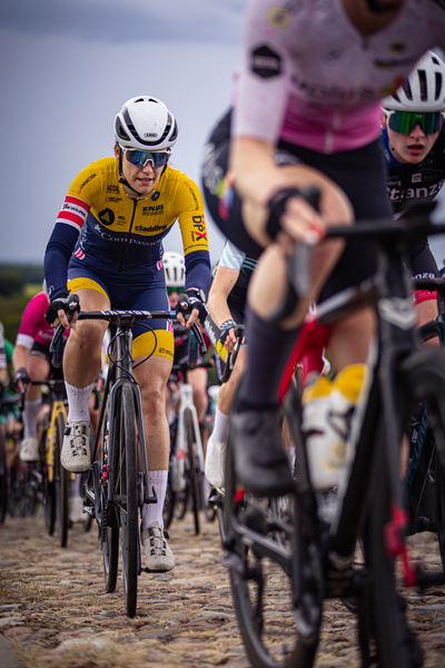 A cyclist wearing a yellow and blue shirt is part of the Nederlands Kampioenschap, Dames Elite ZC team.