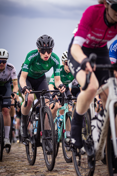 A group of cyclists race in a competition, the cyclist at the front is wearing a green jersey with "Jumbo" written on it.