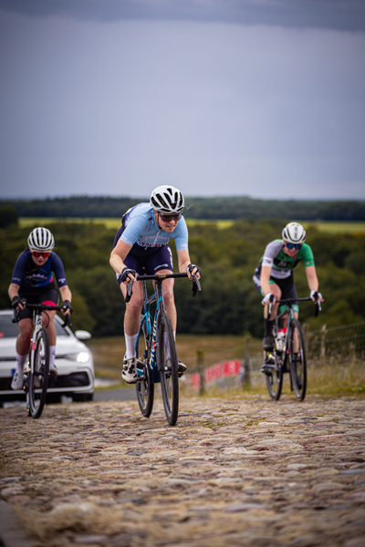 Three cyclists are on a cobblestone road at the Nederlands Kampioenschap.