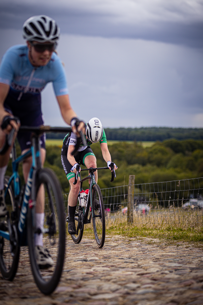 Dames Elite ZC racing cyclist wearing a black and white uniform is riding on a cobblestone road.