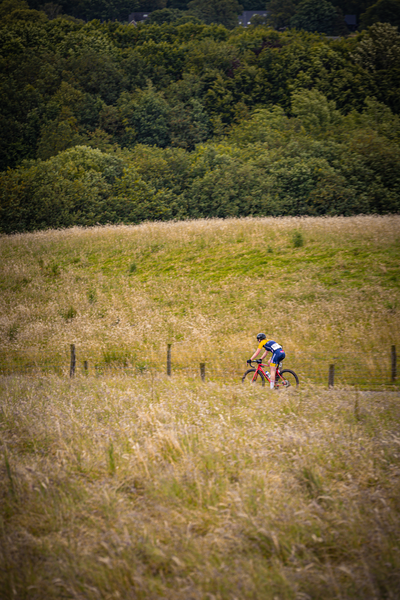 A woman with a blue shirt and a yellow hat riding her bike in the grass.