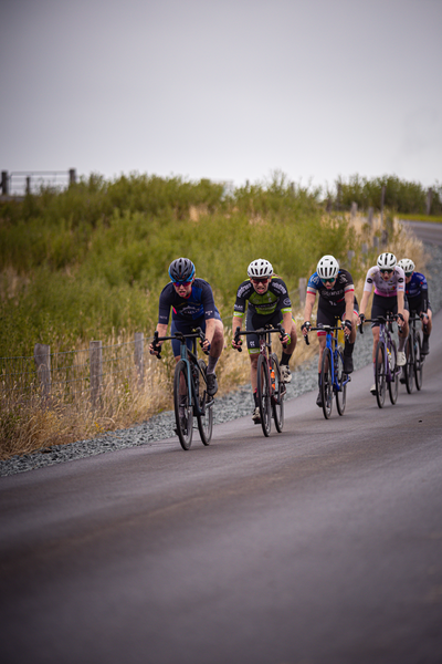 A group of cyclists ride together on a road, with the first cyclist wearing a helmet and riding blue bike.