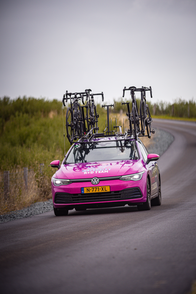 A pink Volkswagen car is transporting multiple bicycles on its roof.