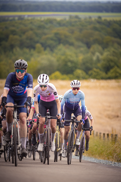 A group of cyclists race on a street. The leader wears a blue jersey and the number 3.