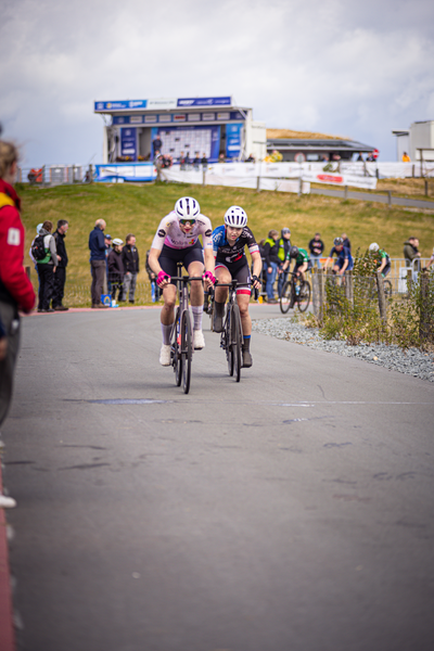 Two cyclists are riding down a street during the Nederlands Kampioenschap.