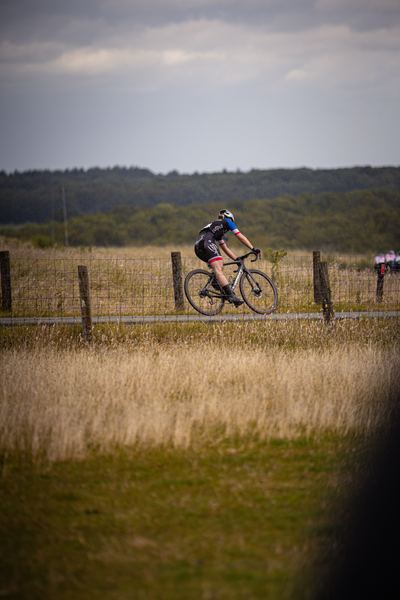 A bicycle racer in front of a fence and grassy field.