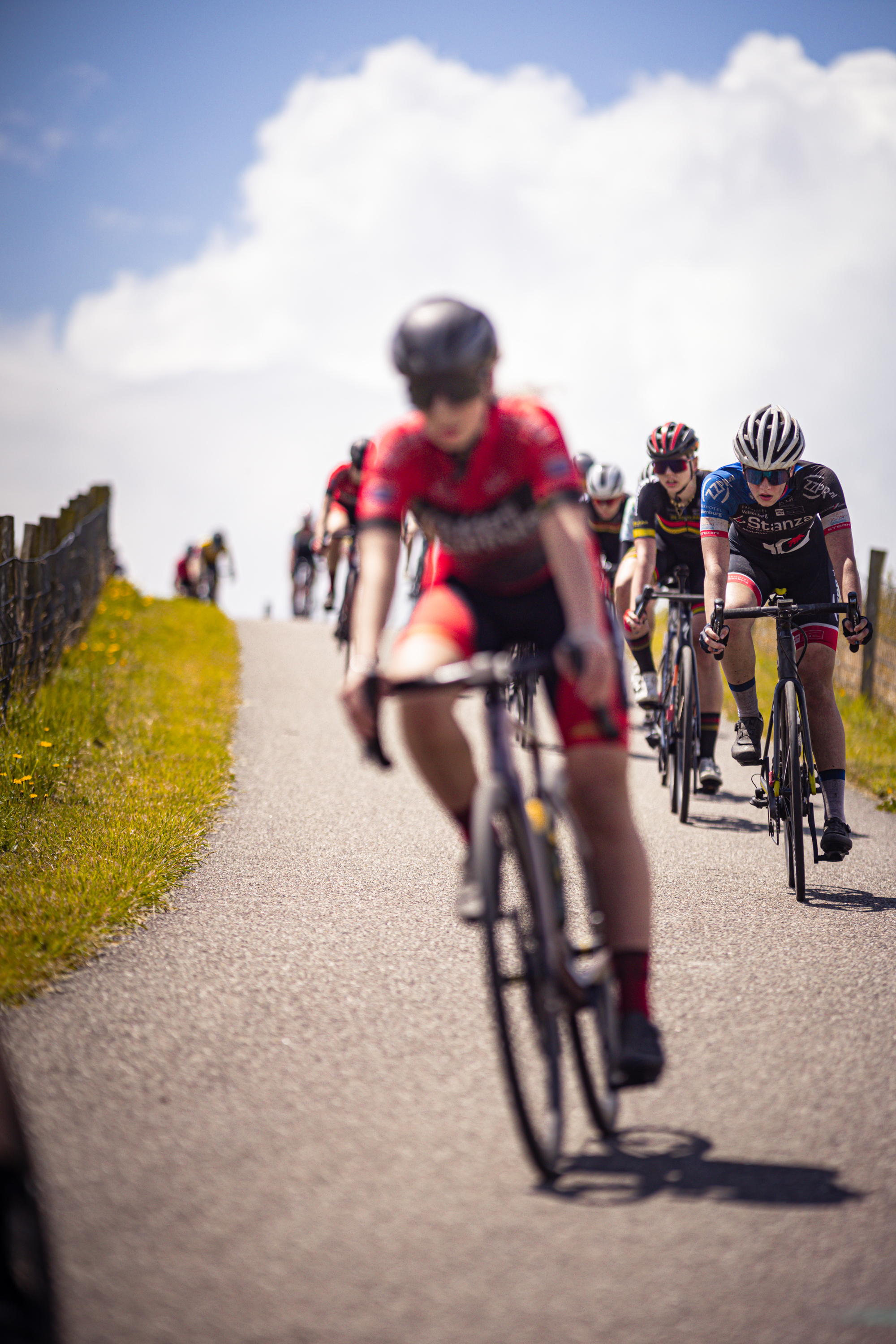 Several cyclists are riding along a road, preparing to take part in the Nederlands Kampioenschap.