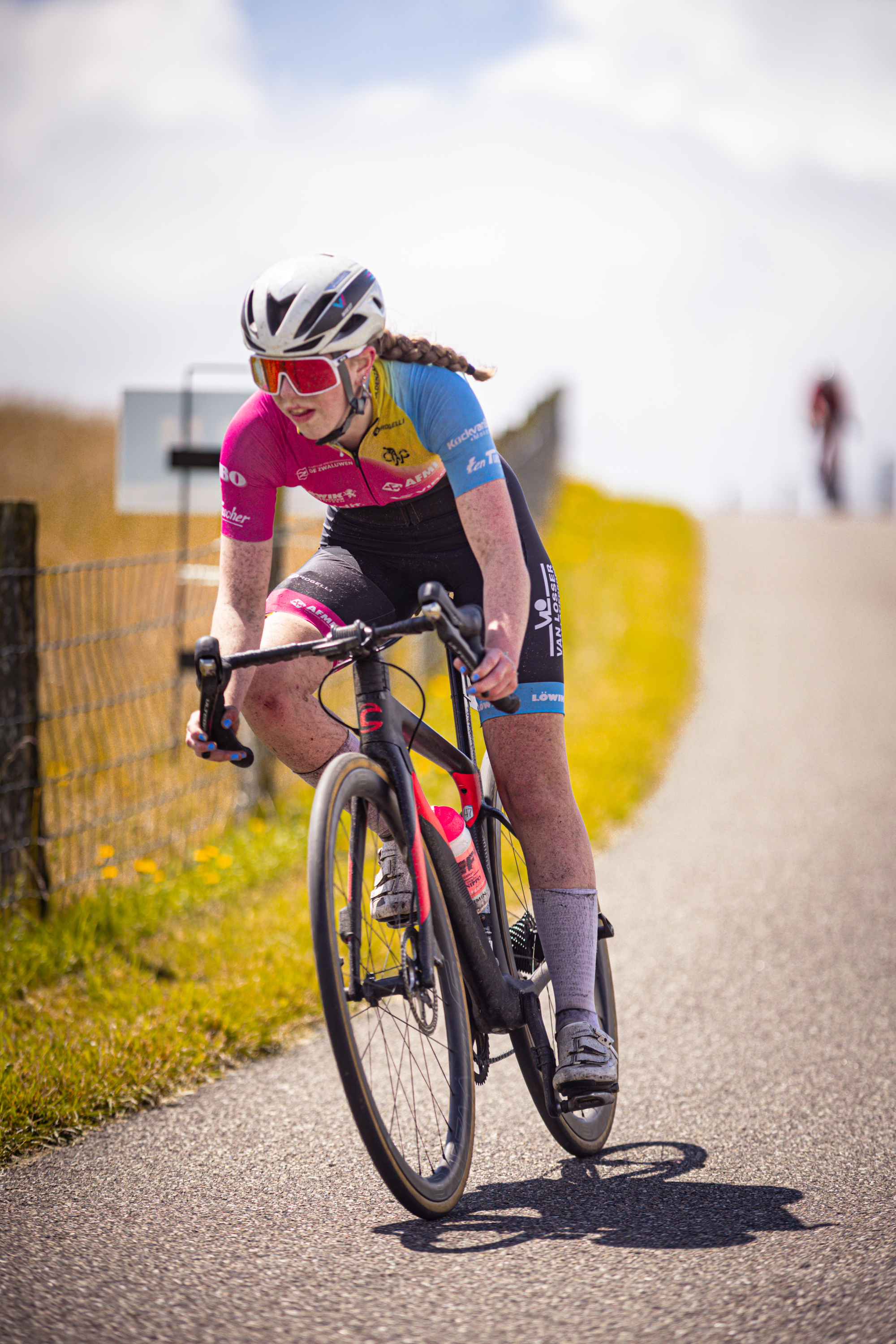 A cyclist in a pink and blue jersey is riding on a road.