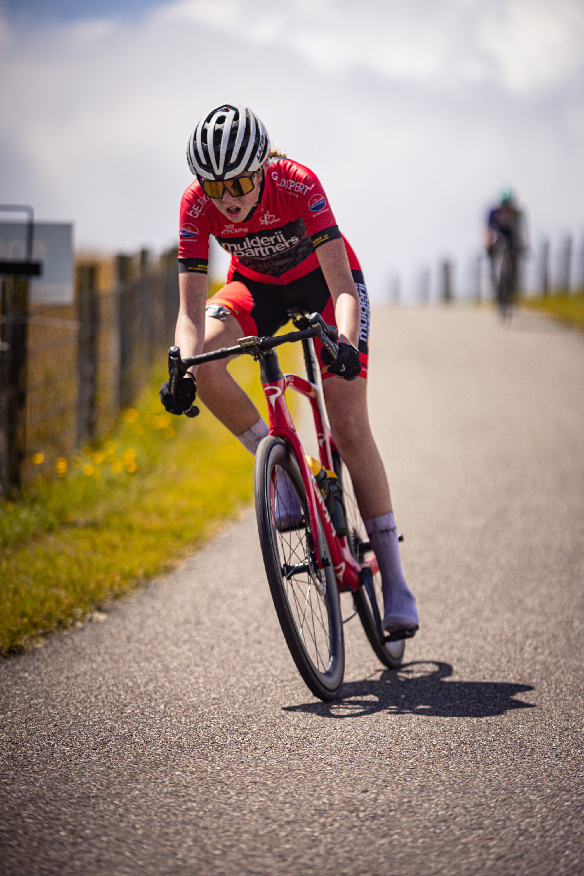 A bicyclist in a red shirt and black helmet is riding down a road.