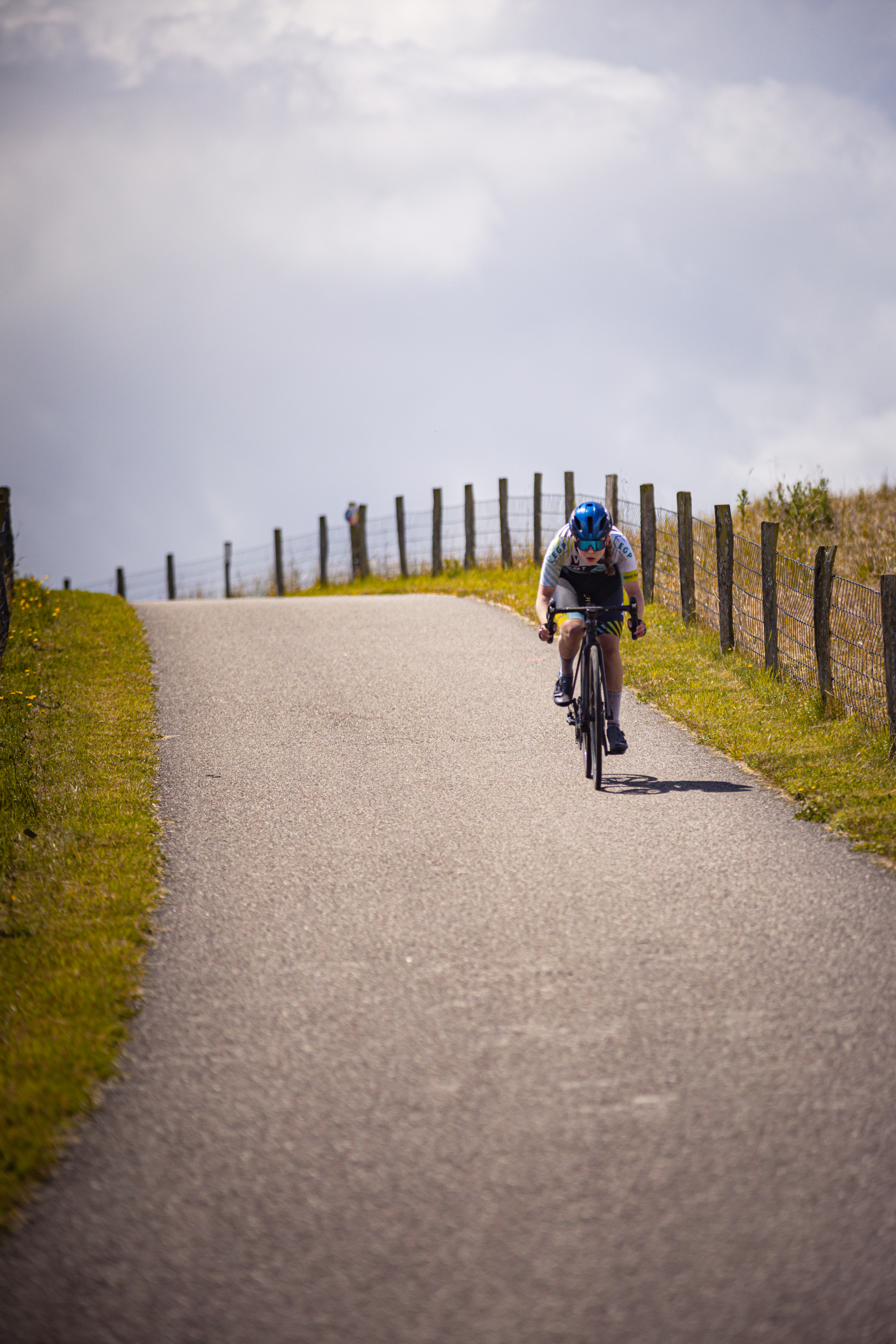 A cyclist wearing a blue helmet rides her bike on the road.