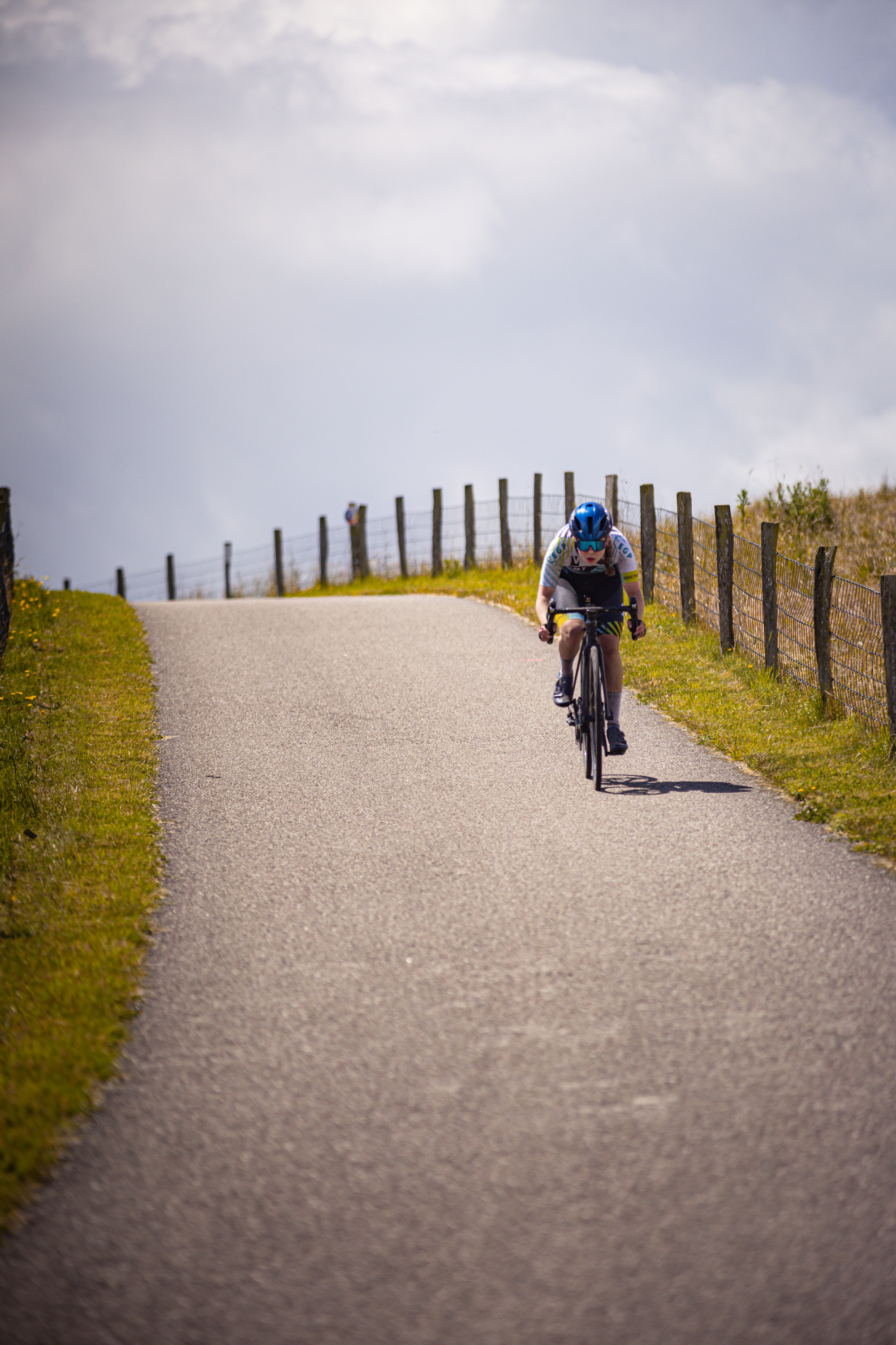 A cyclist wearing a blue helmet rides her bike on the road.