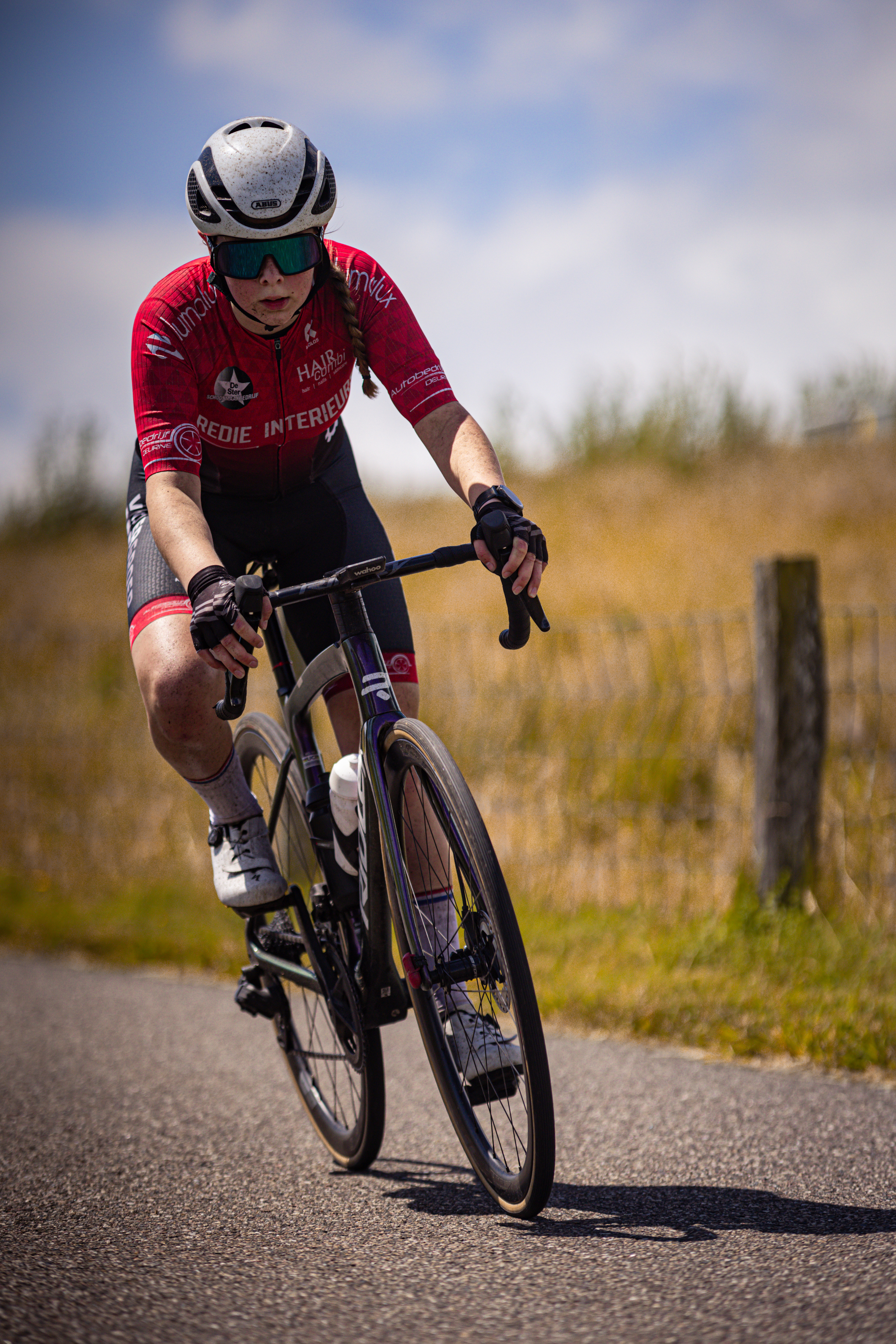 A man wearing a red shirt with the number 2024 on it. He is riding a bicycle down a road next to a fence.