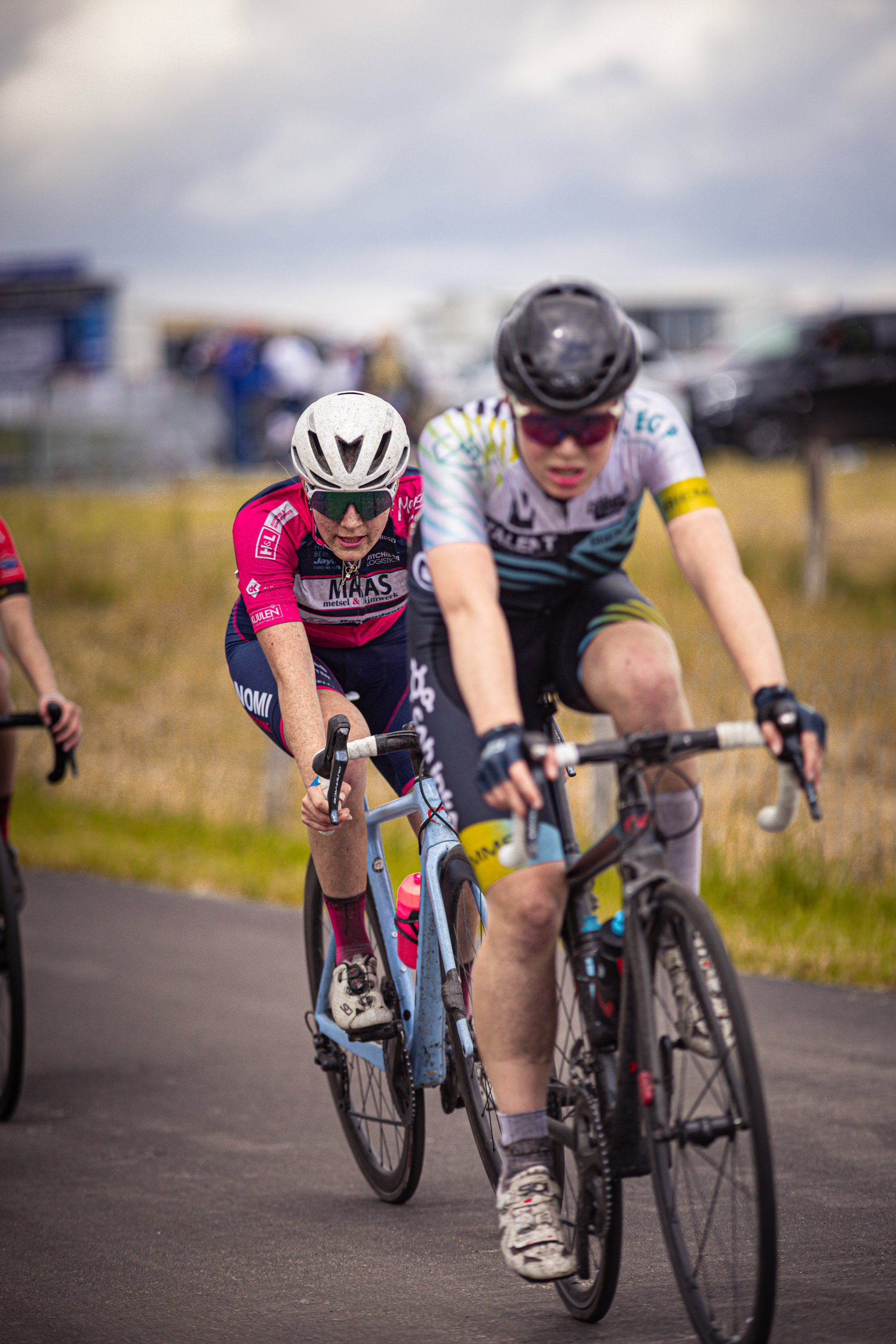 Two people on bikes wearing white helmets in a competition.