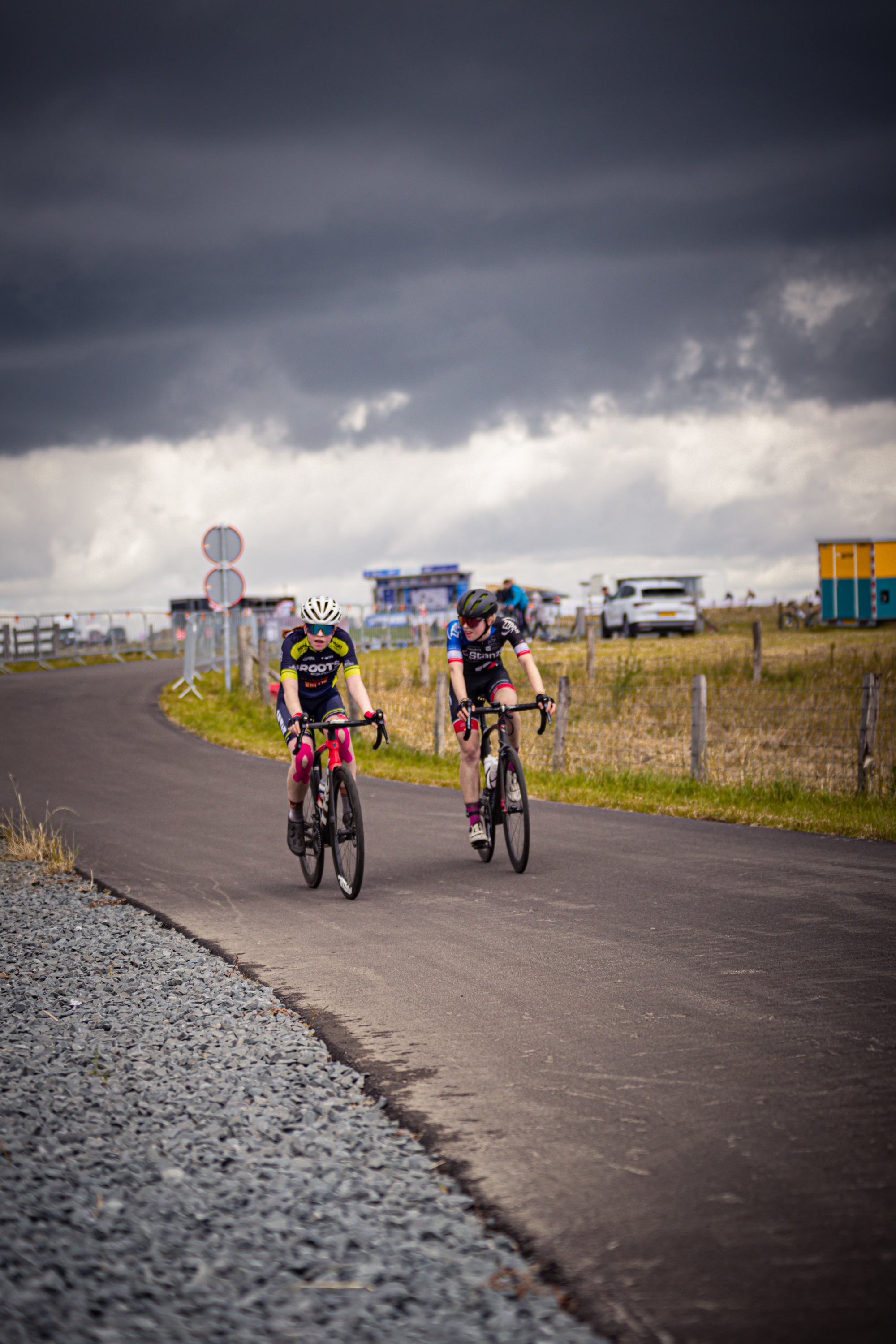 Two cyclists are riding down a road with one wearing a number 14 jersey.