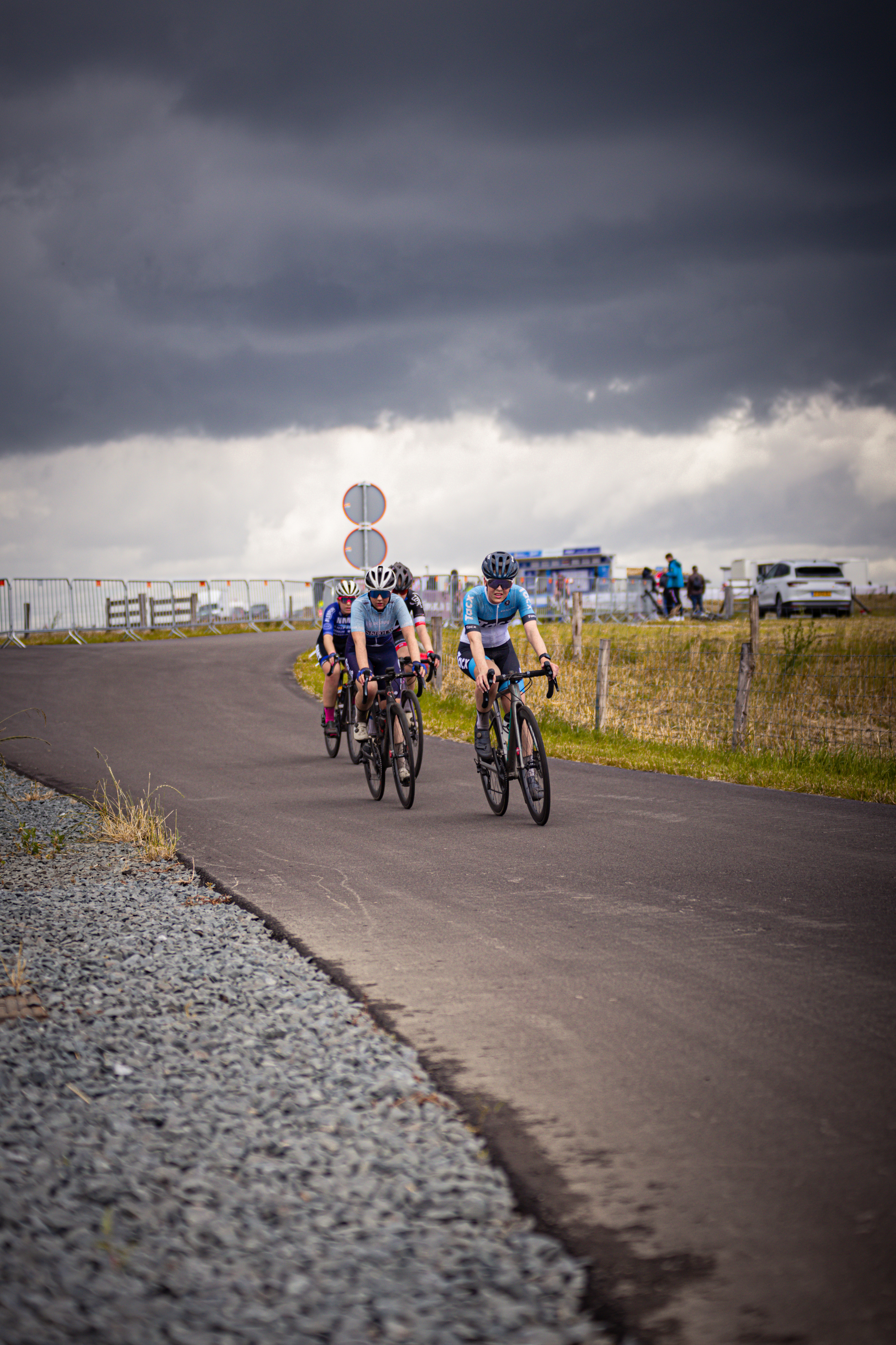 Three cyclists riding down the road, with one leading and two following.