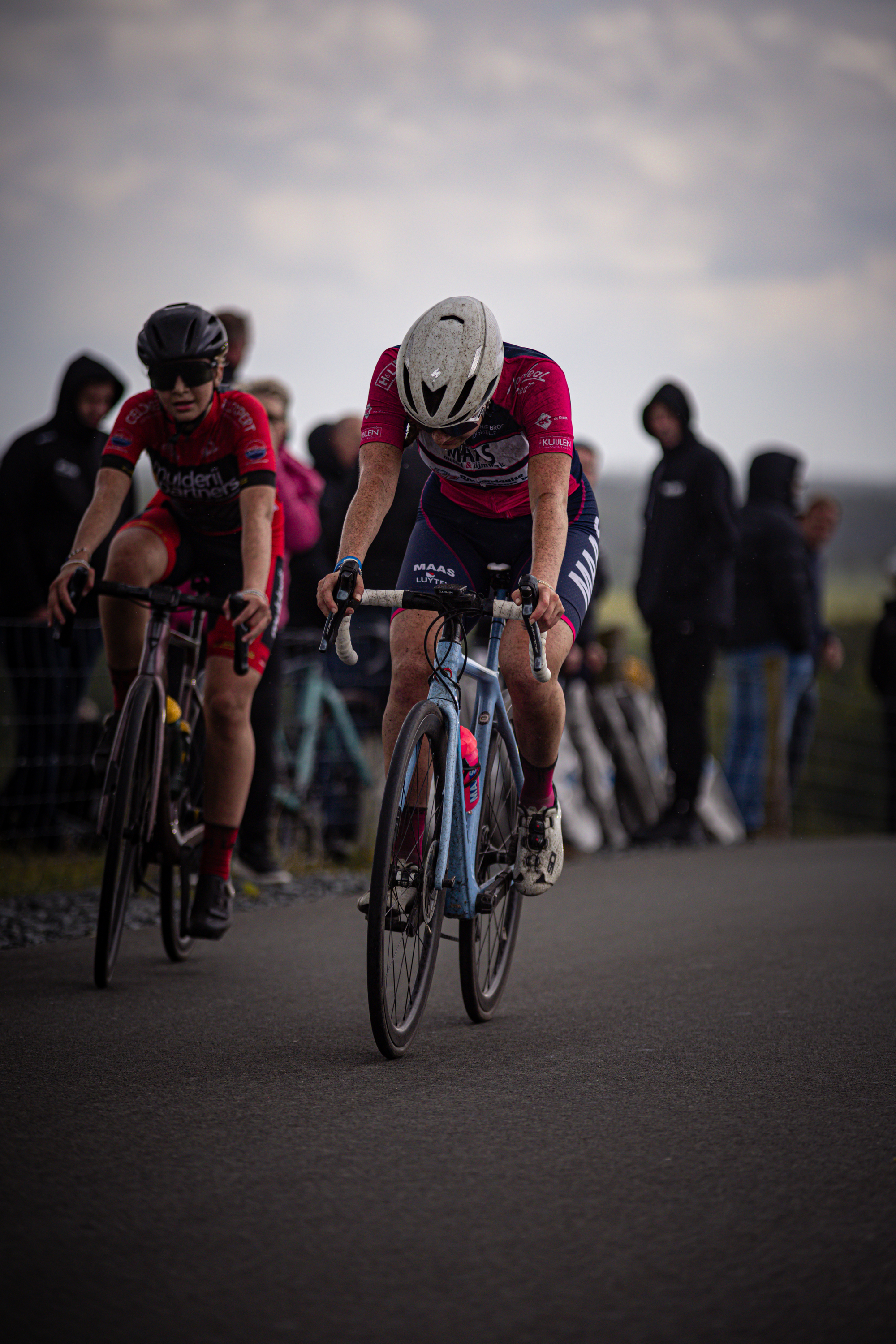 Two women are riding bikes in a group race. One is wearing a pink jersey and the other is wearing red, blue and black.