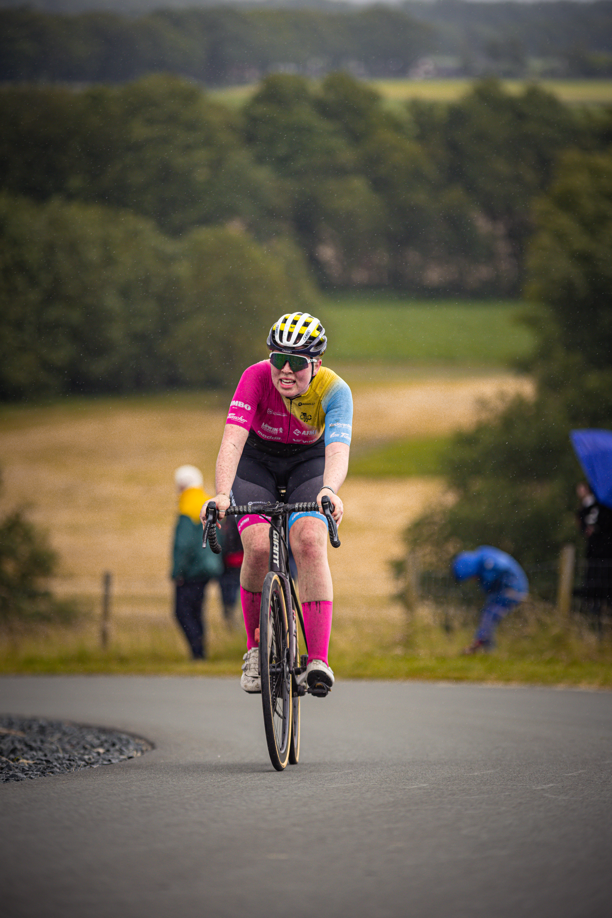 A woman wearing a pink jersey and helmet rides her bike down the street.