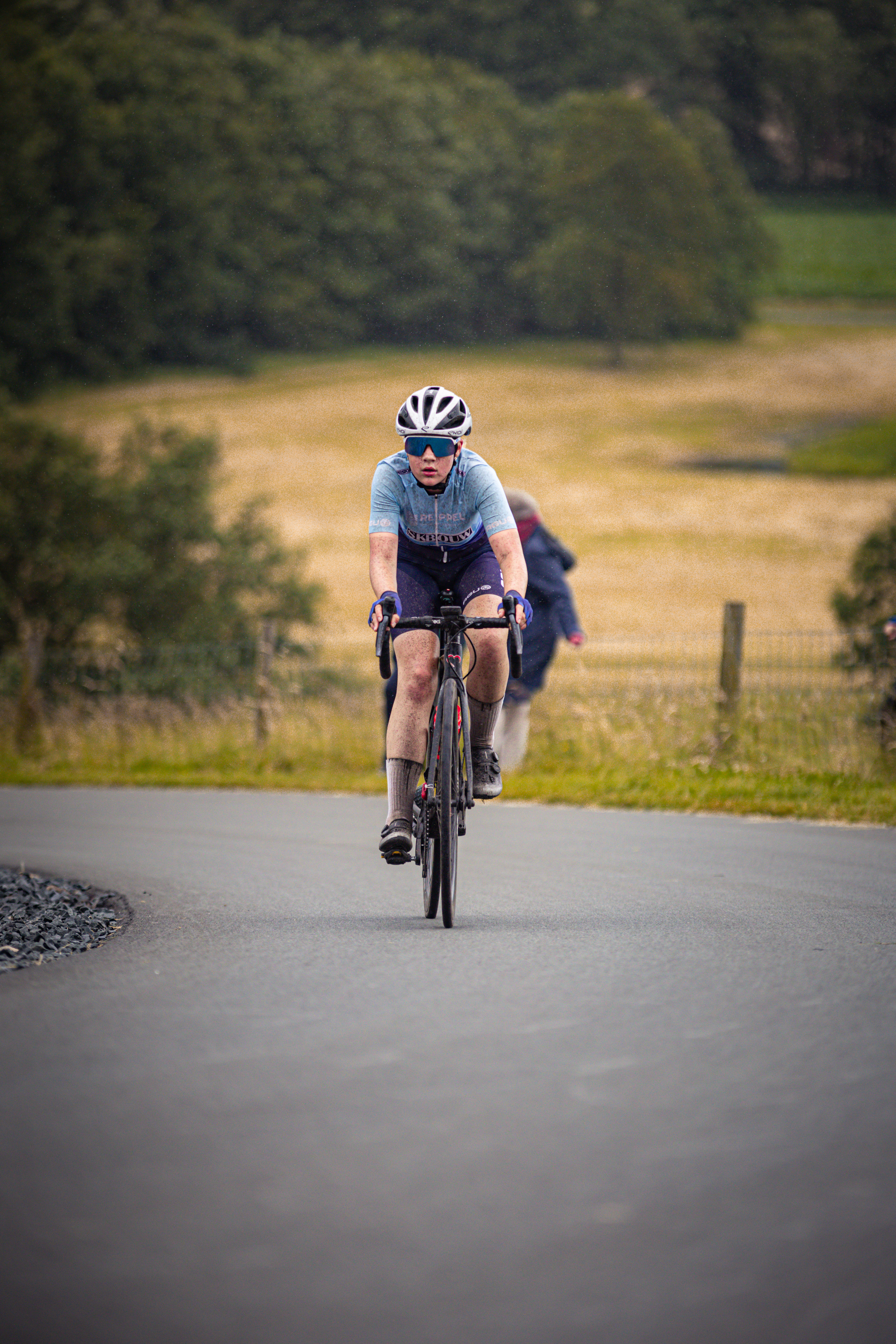 A person riding a bike on a road with an arched sign behind them that says "Wielrennen".