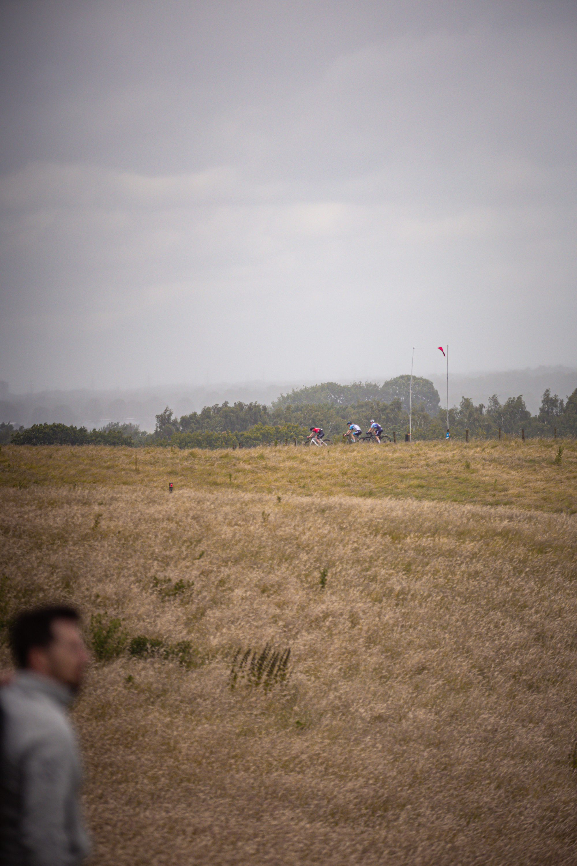 A cyclist wearing a blue helmet pedals through the countryside on a cloudy day.