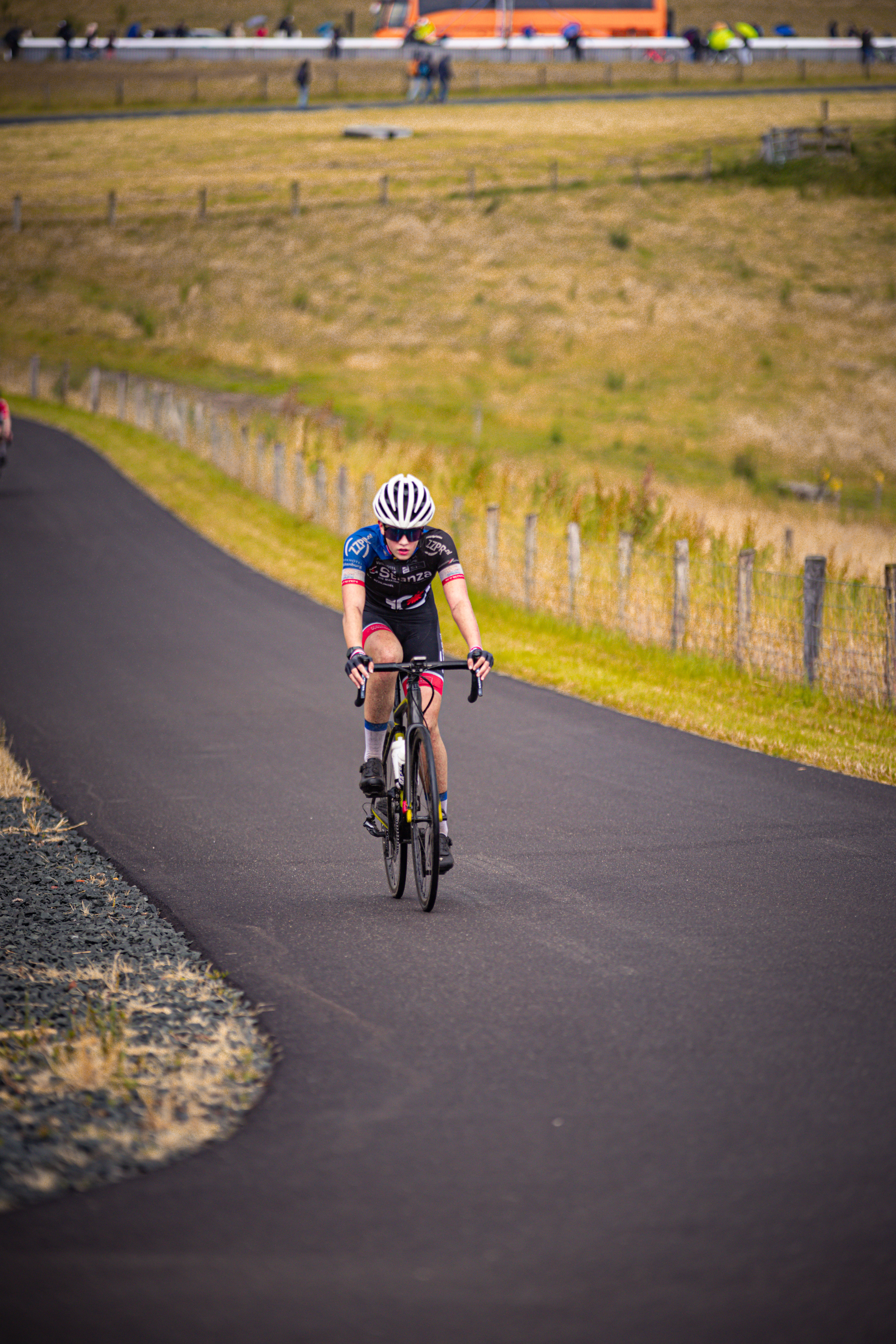 A person riding a bike on an asphalt road with grass and shrubs in the background.