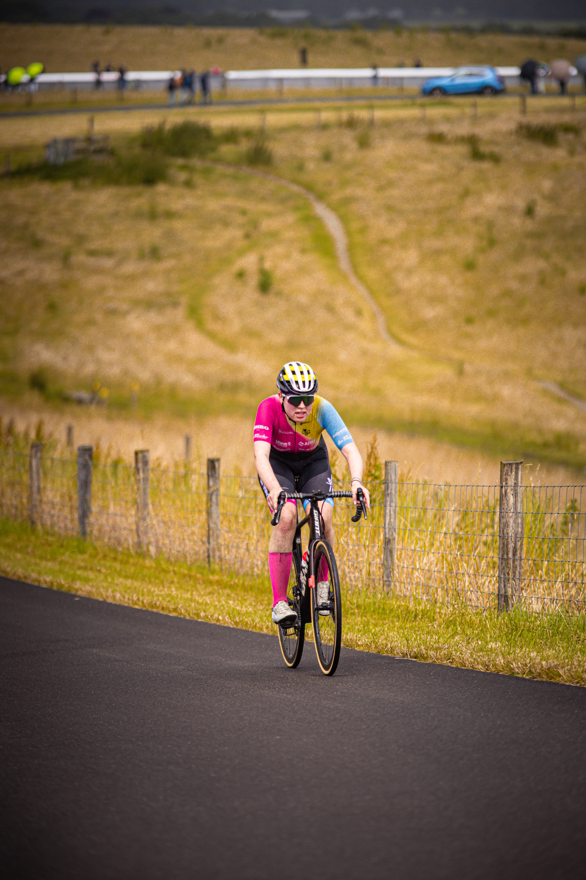 A cyclist in a pink and blue jersey rides on a rural road.