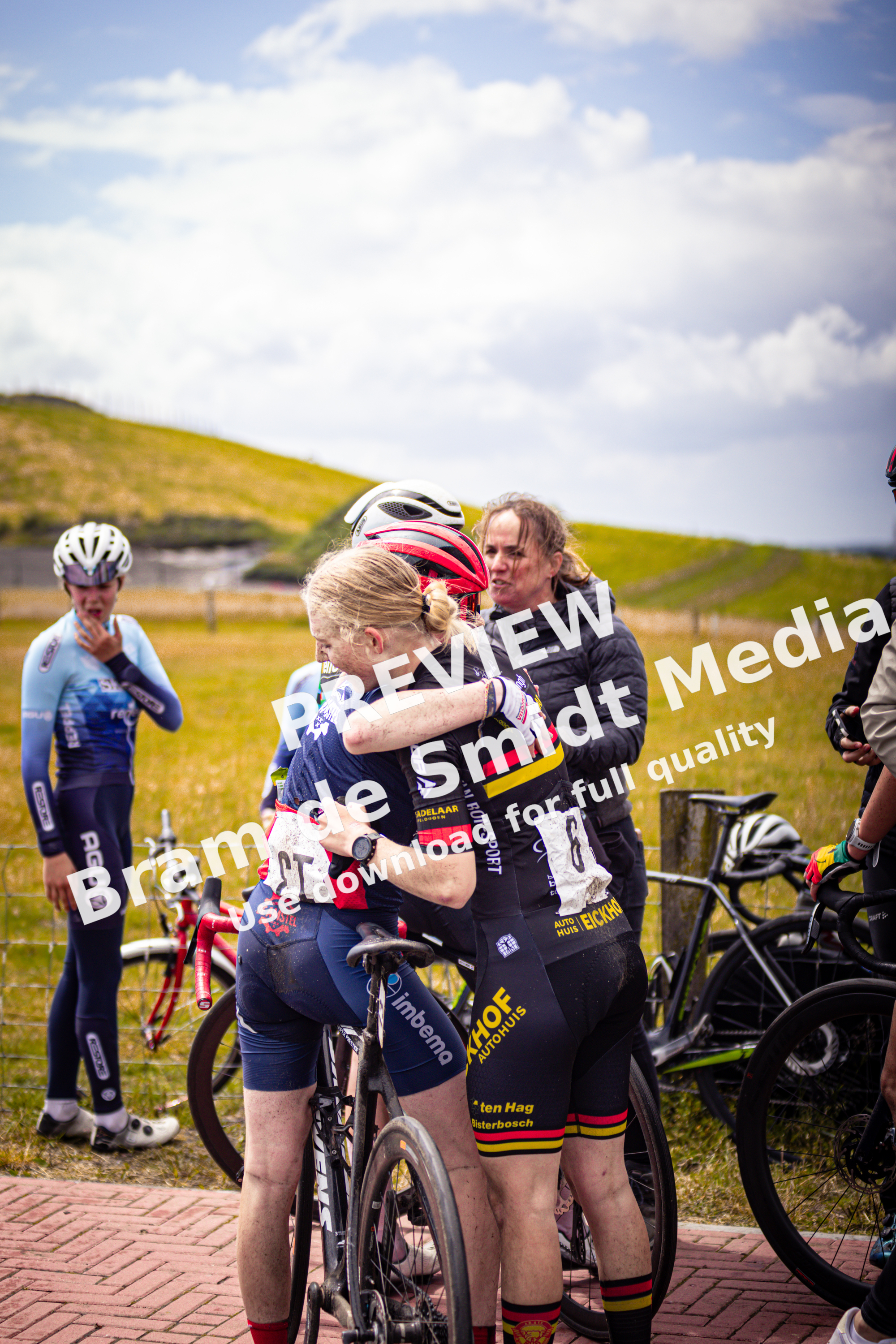 Two women, wearing matching red and black uniforms with the word "Bouwen" on them, hug each other.