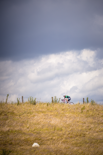 A woman is riding a bike on a grassy hill on a stormy day.